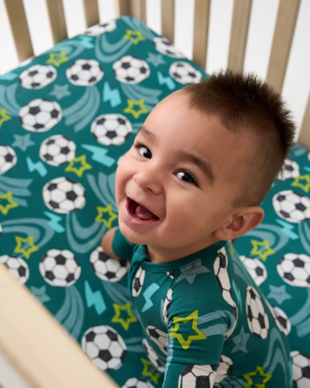 Baby sitting in a crib with the Soccer Stars Fitted Crib Sheet