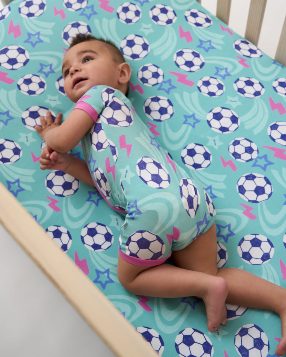 Baby laying on the Aqua Soccer Stars Fitted Crib Sheet in a matching Zippy