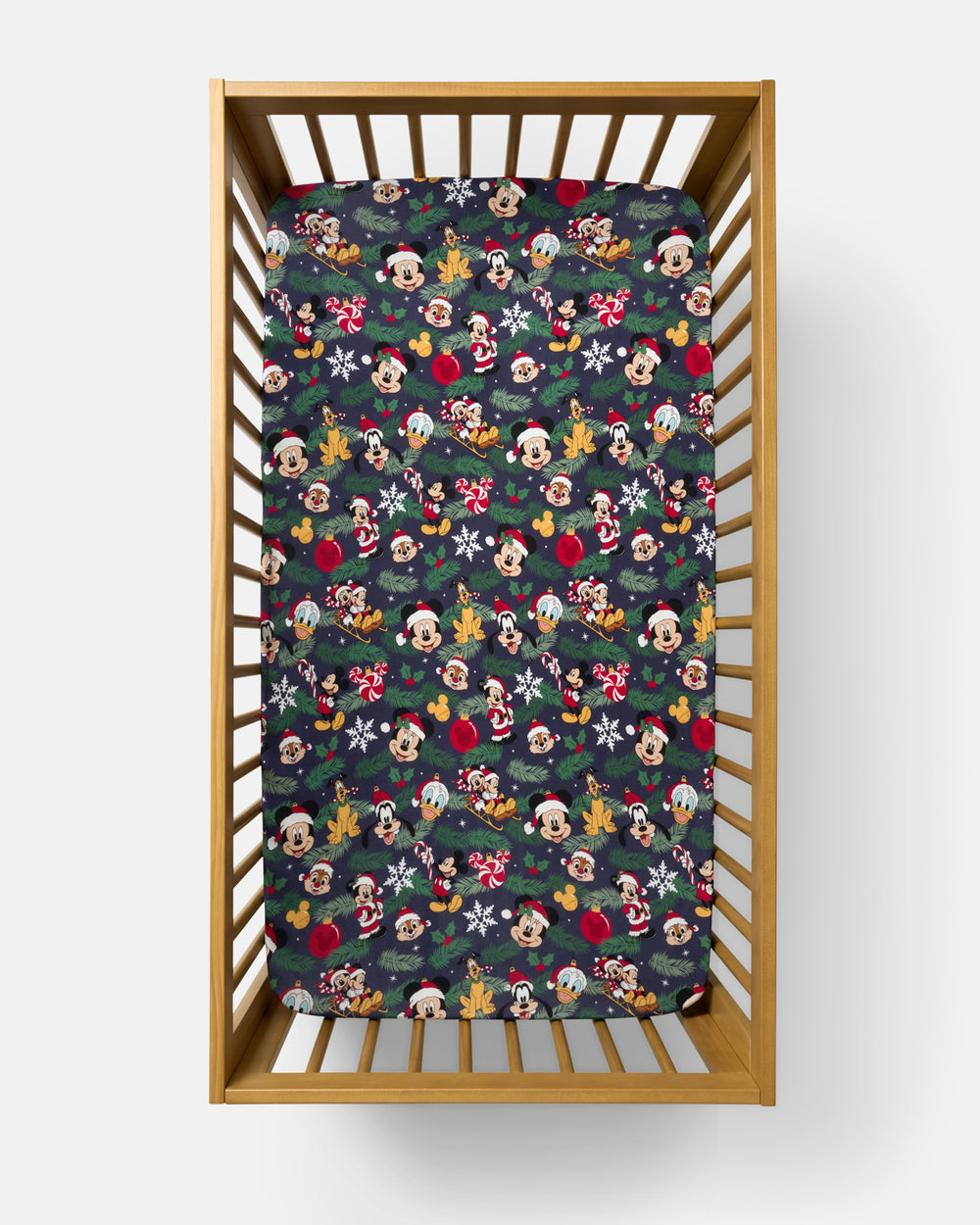 A fitted crib mattress with a festive Disney Christmas print, shown inside a light wood crib on a clean white background.