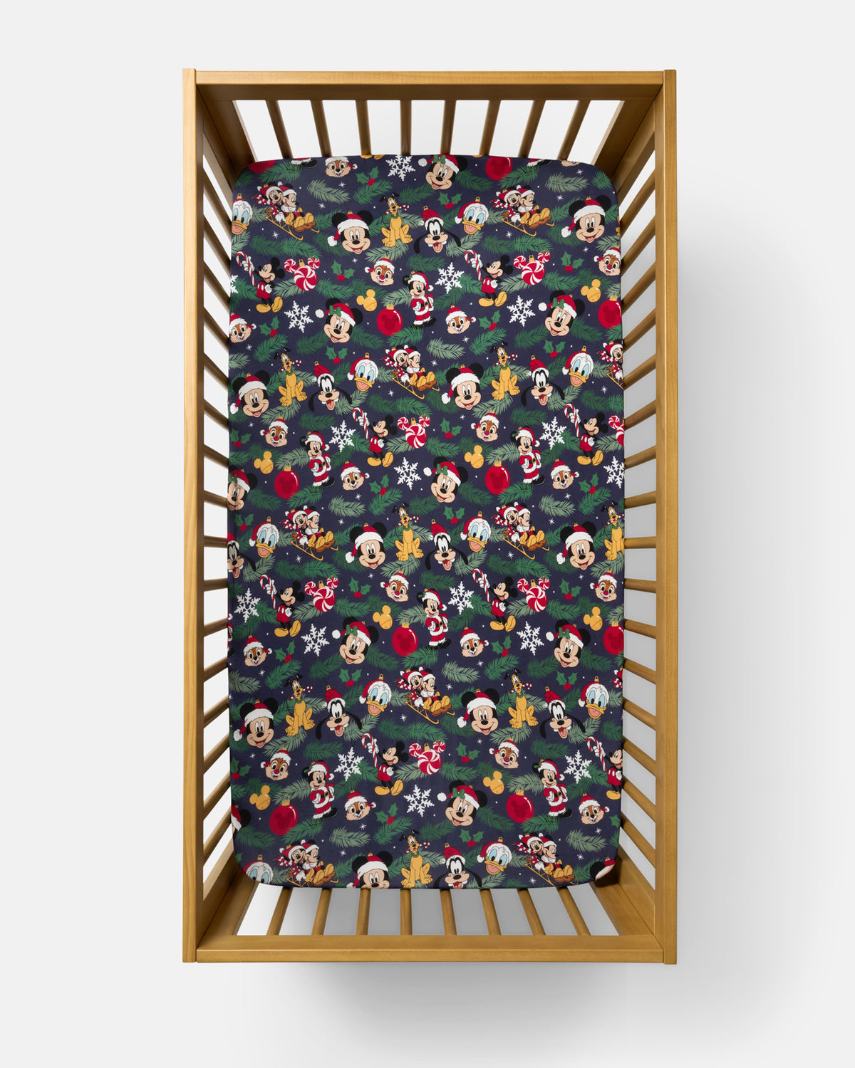 A fitted crib mattress with a festive Disney Christmas print, shown inside a light wood crib on a clean white background.