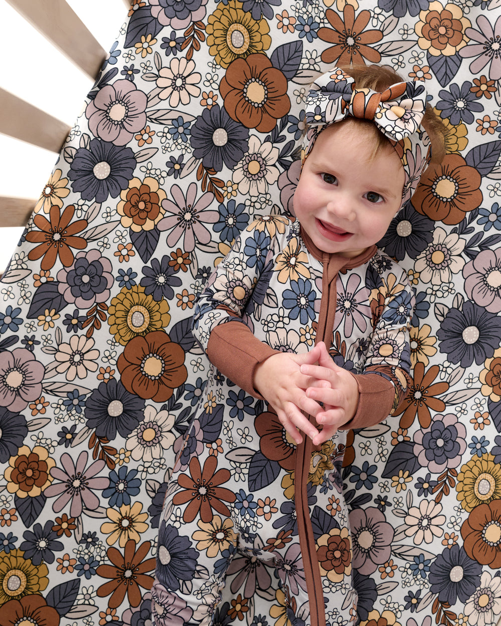 Baby laying on the Wildwood Floral Fitted Crib Sheet wearing a matching zippy