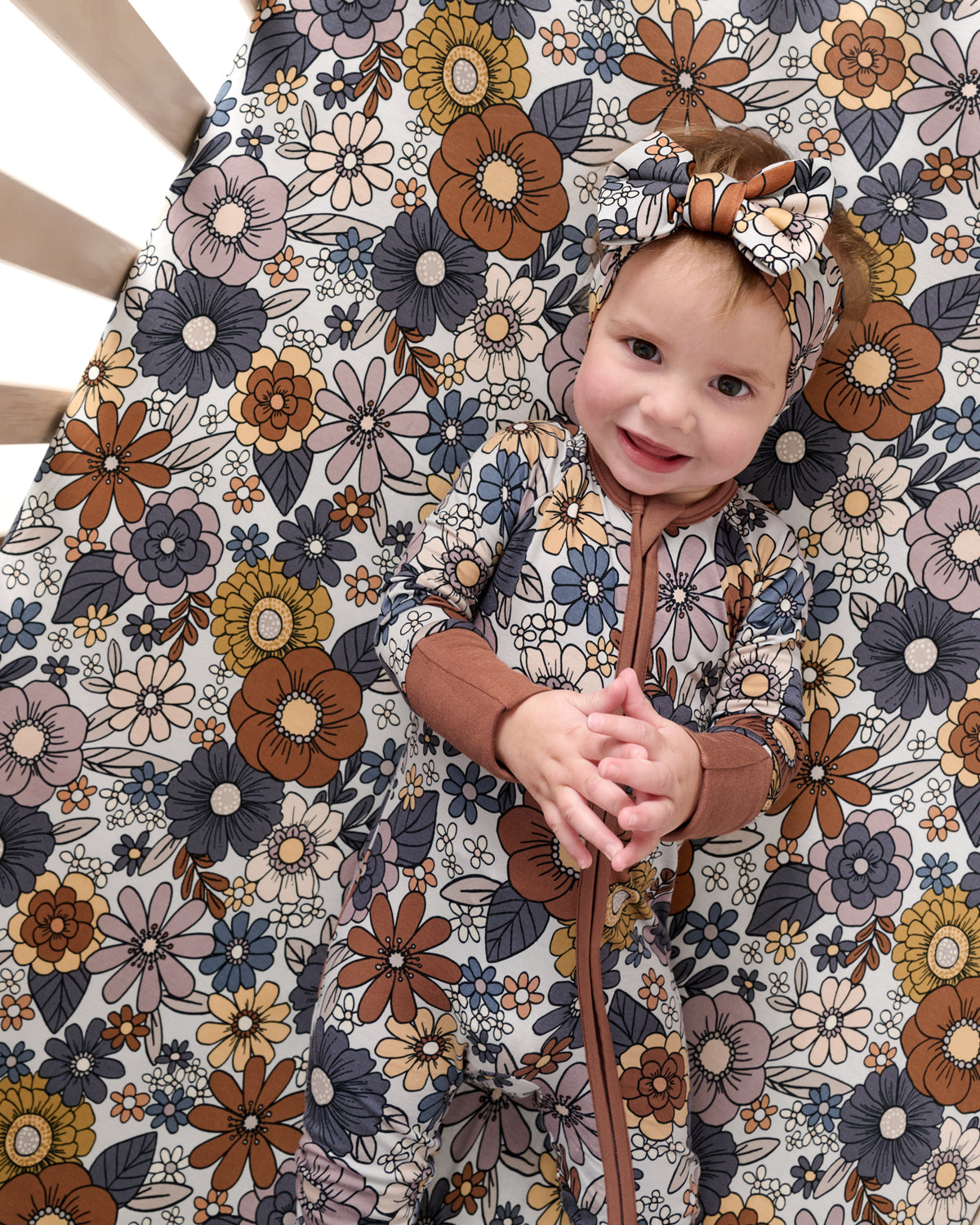 Baby laying on the Wildwood Floral Fitted Crib Sheet wearing a matching zippy