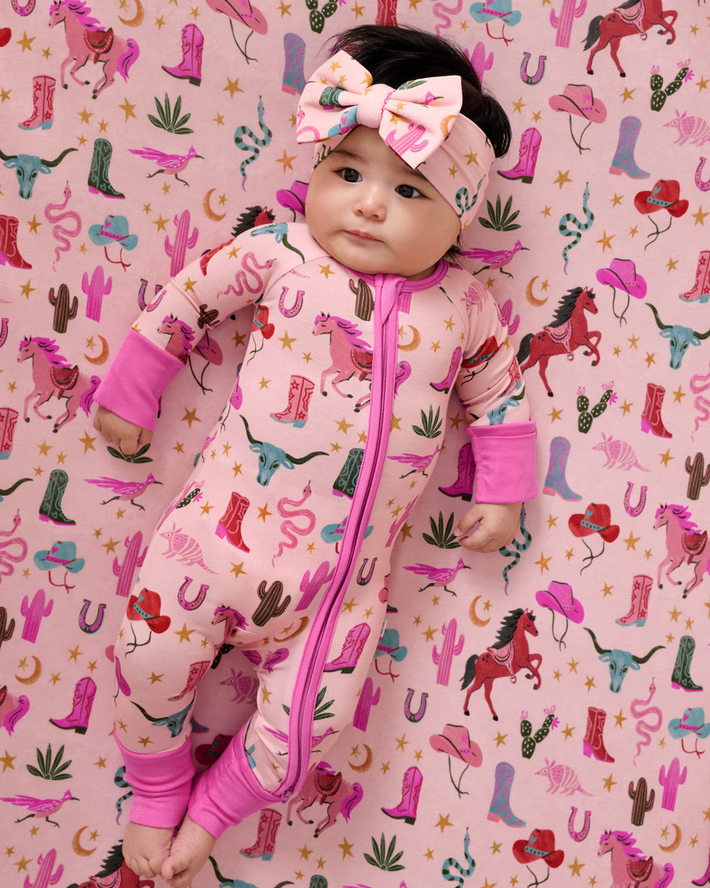 Close up overhead view of baby laying on the Pink Rancher Roundup Fitted Crib Sheet in a matching zippy
