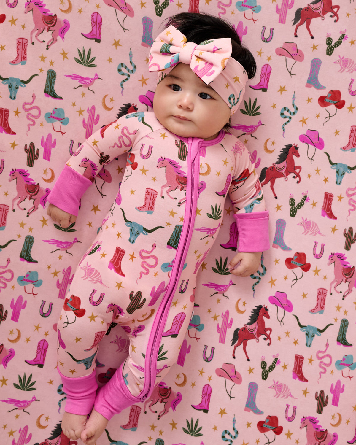 Close up overhead view of baby laying on the Pink Rancher Roundup Fitted Crib Sheet in a matching zippy