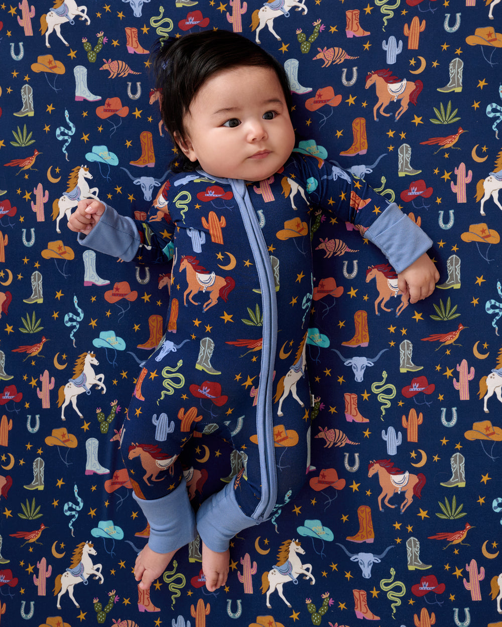 Baby laying on the Blue Rancher Roundup Fitted Crib Sheet in a matching zipper pajama