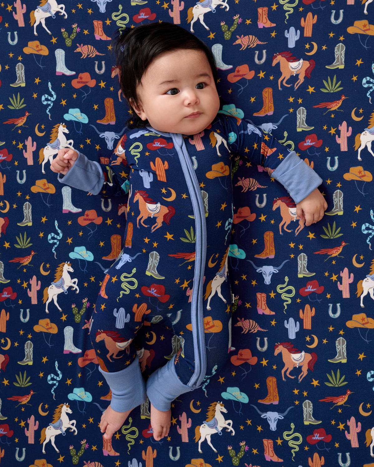 Baby laying on the Blue Rancher Roundup Fitted Crib Sheet in a matching zipper pajama