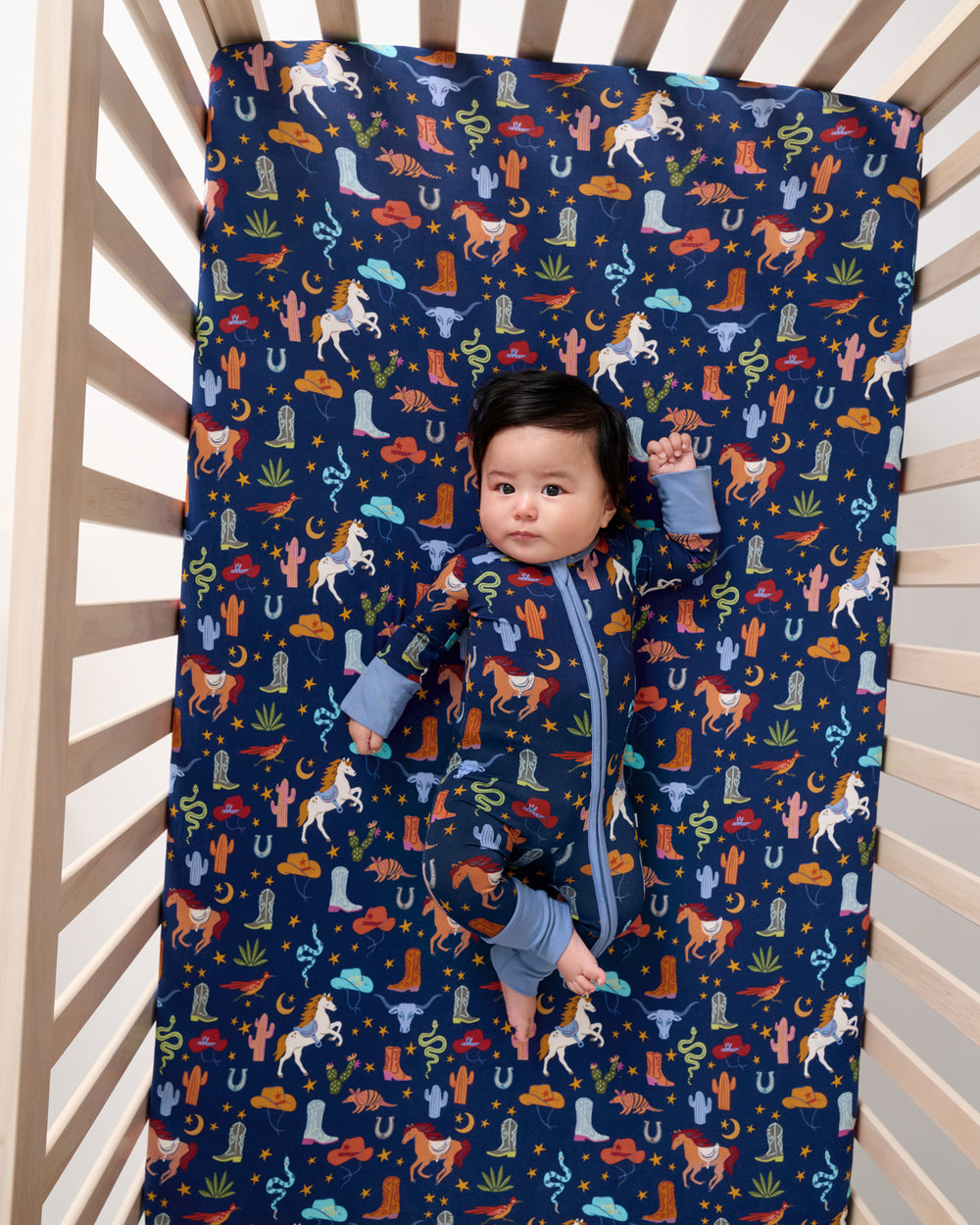 Overhead view of baby laying on the Blue Rancher Roundup Fitted Crib Sheet