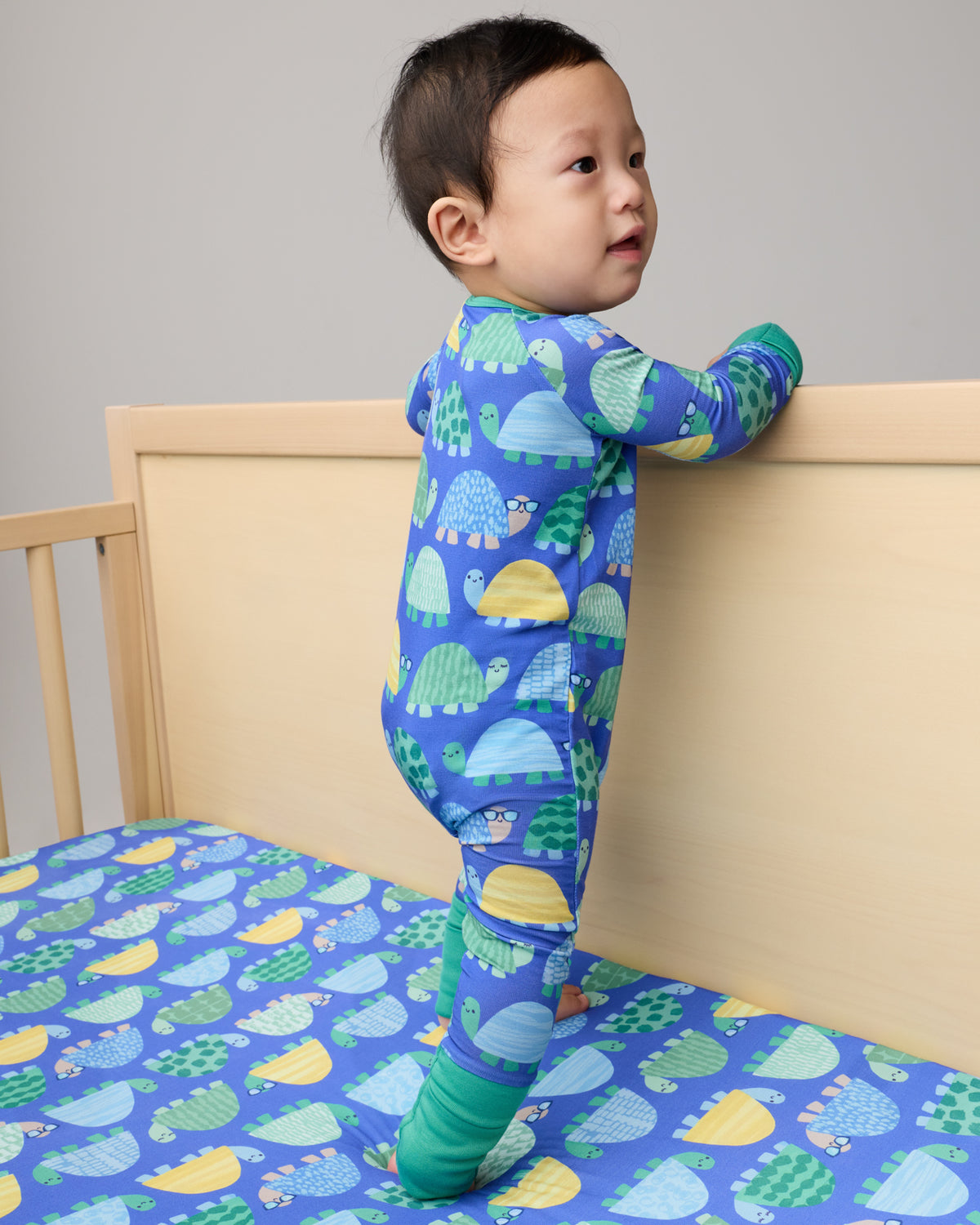 Baby standing in a crib with the Shell Parade Fitted Crib Sheet