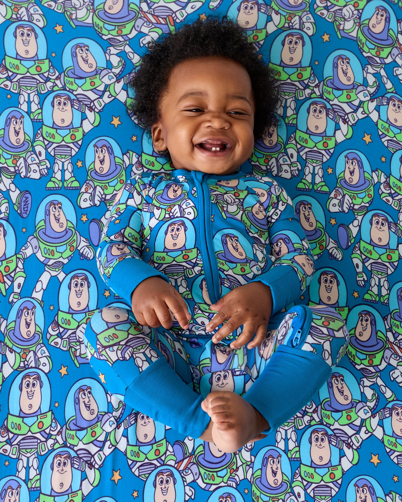 Baby laying on the Disney & Pixar Buzz's Cosmic Crew Fitted Crib Sheet in a matching zippy