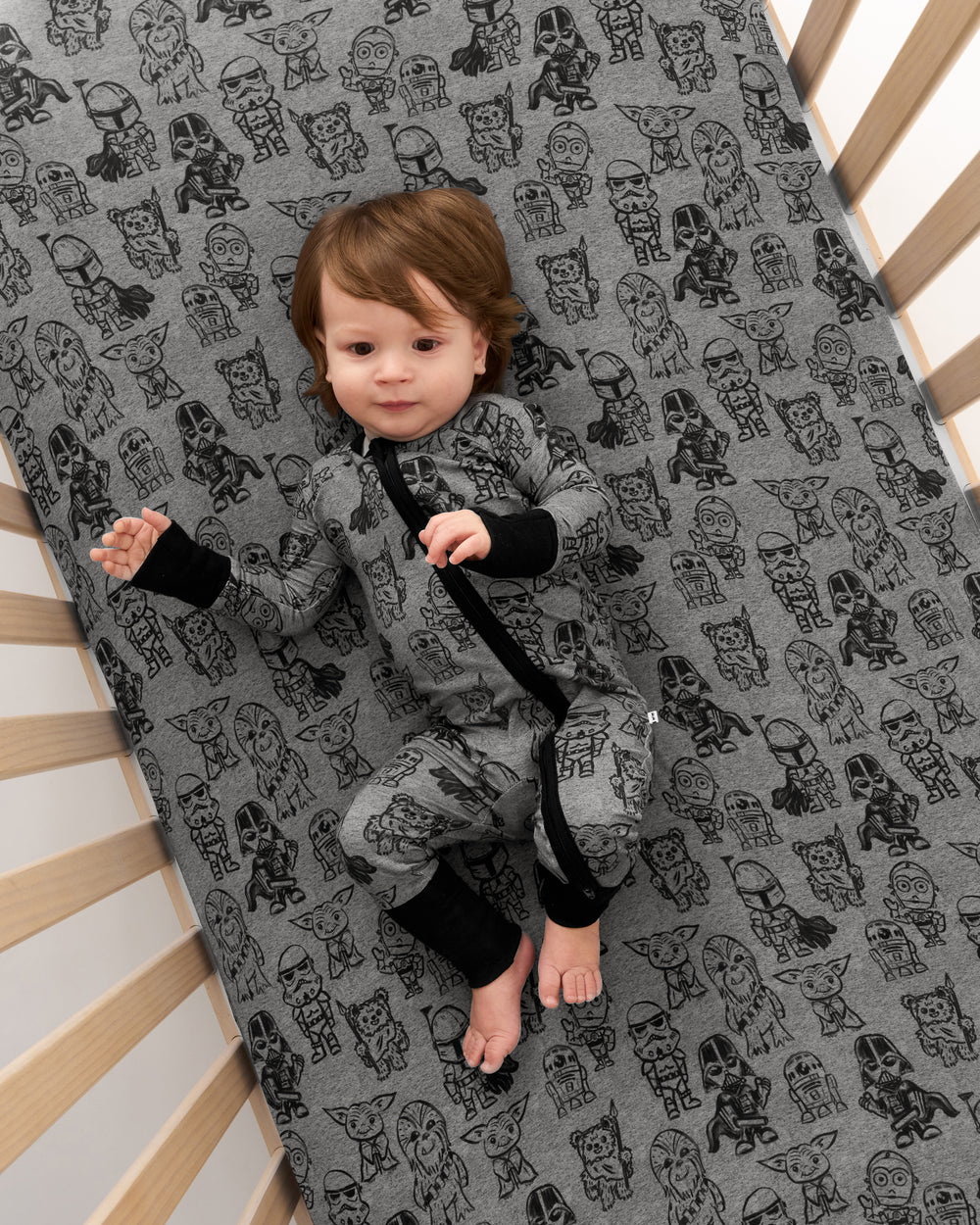 Overhead view of baby laying on the Star Wars Far, Far, Away Friends Fitted Crib Sheet wearing the matching Zippy