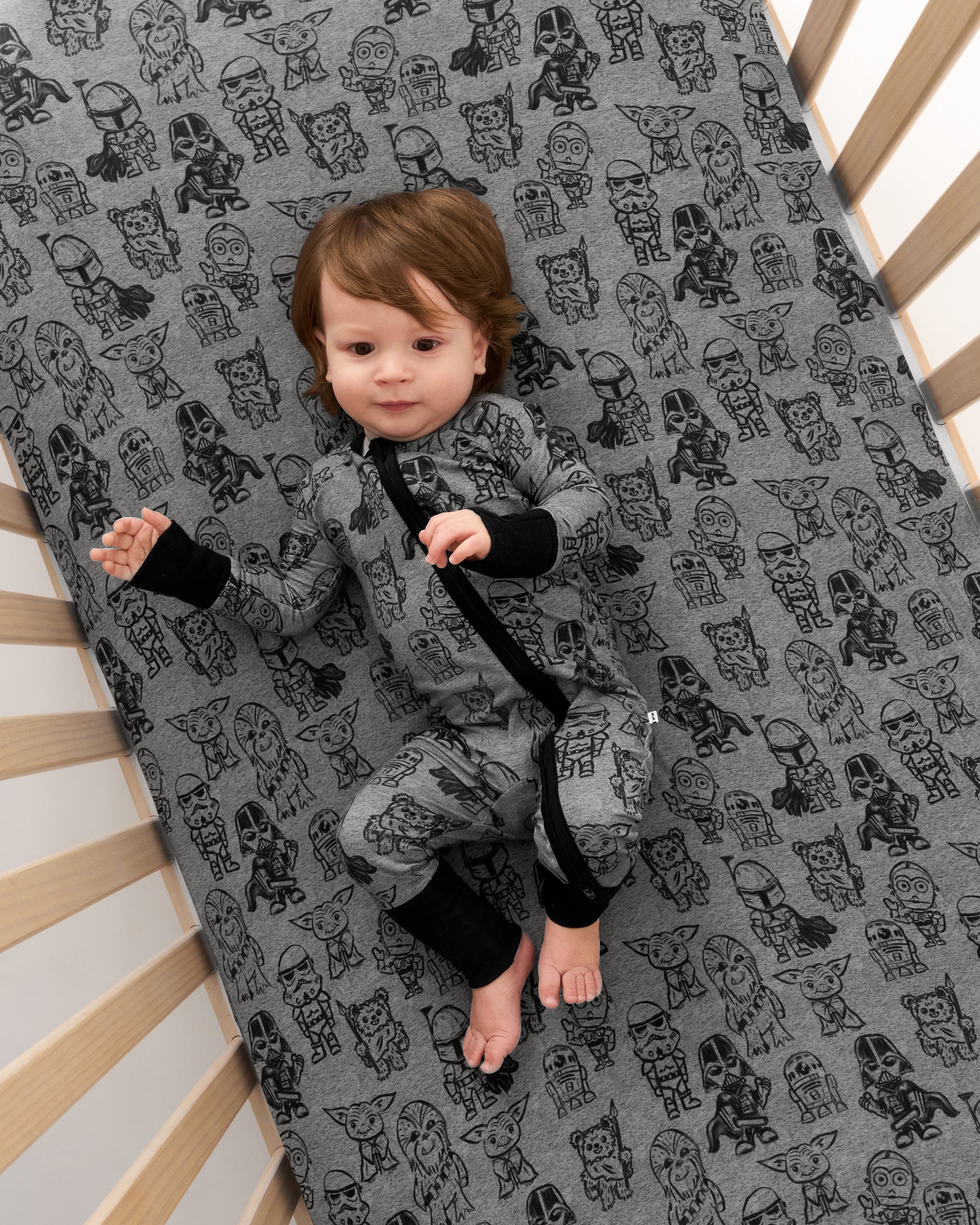 Overhead view of baby laying on the Star Wars Far, Far, Away Friends Fitted Crib Sheet wearing the matching Zippy