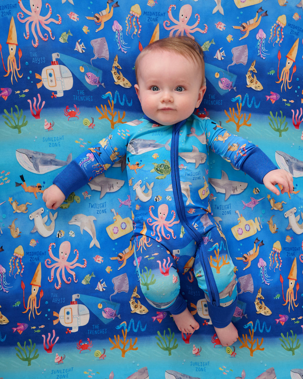 Overhead view of baby laying on the Underwater Discovery Fitted Crib Sheet in a matching footie pajama