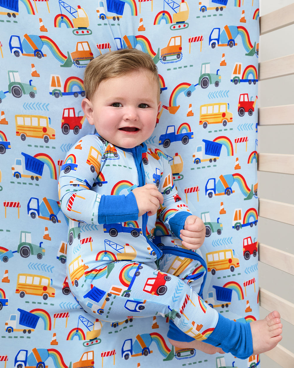 Baby laying on the Rainbow Trucks Fitted Crib Sheet in a matching footie pajama