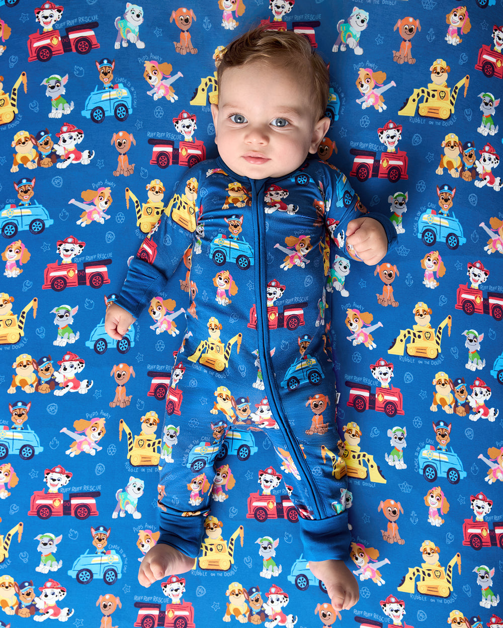 Baby laying on the PAW Patrol Adventure Bay Heroes Fitted Crib Sheet in a matching zippy