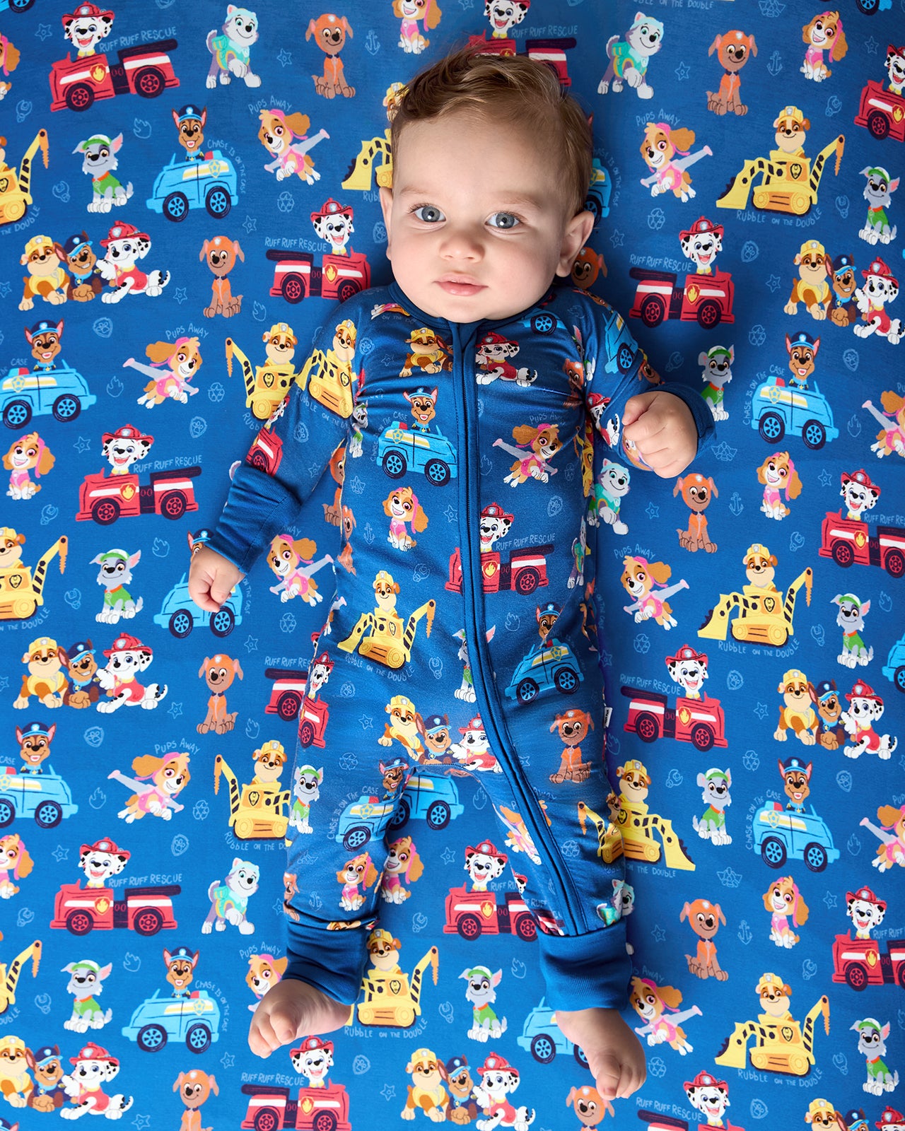 Baby laying on the PAW Patrol Adventure Bay Heroes Fitted Crib Sheet in a matching zippy