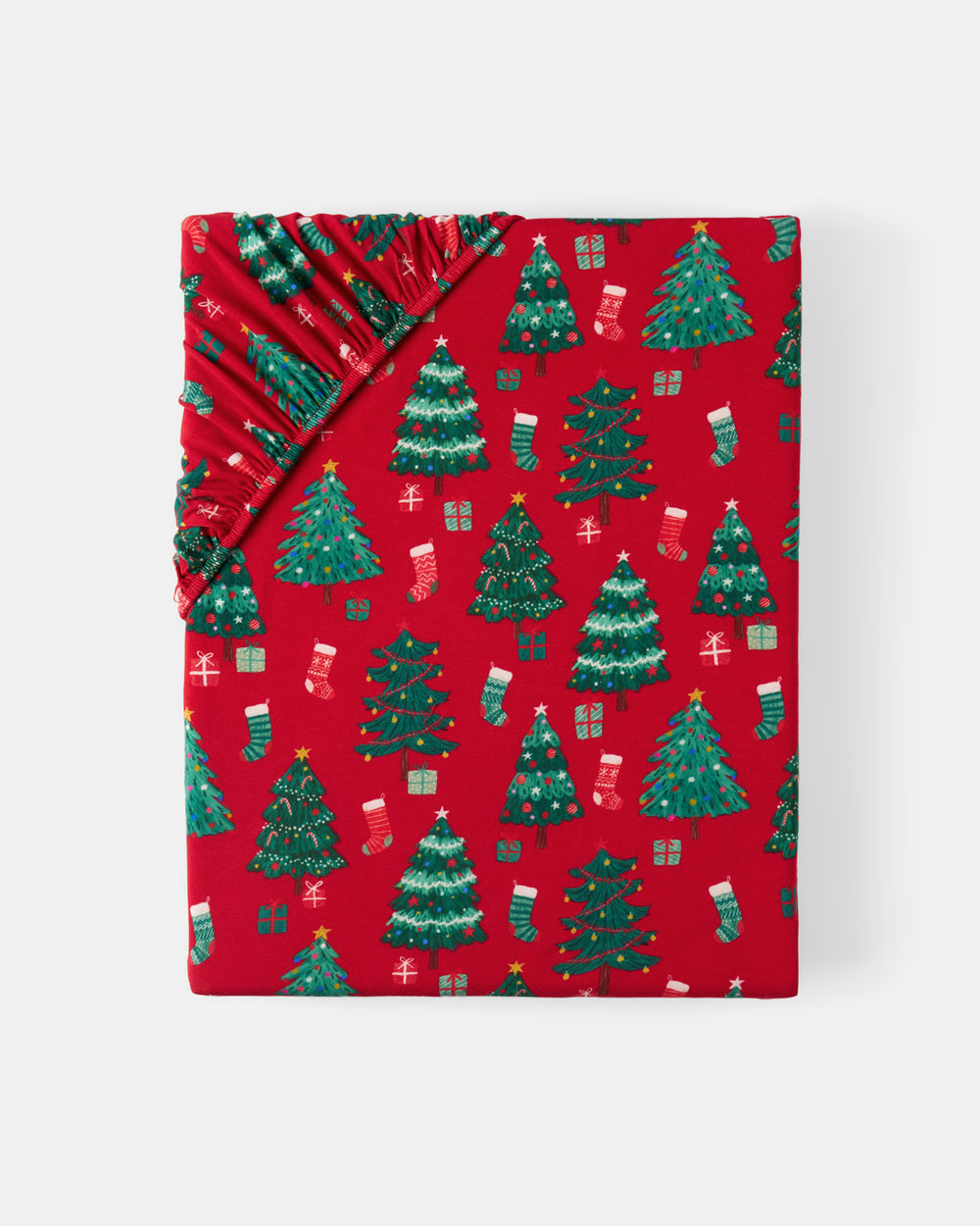 Red wrapping paper with a festive Christmas pattern featuring green Christmas trees, stockings, and presents, shown folded with a gathered top edge on a light gray background.