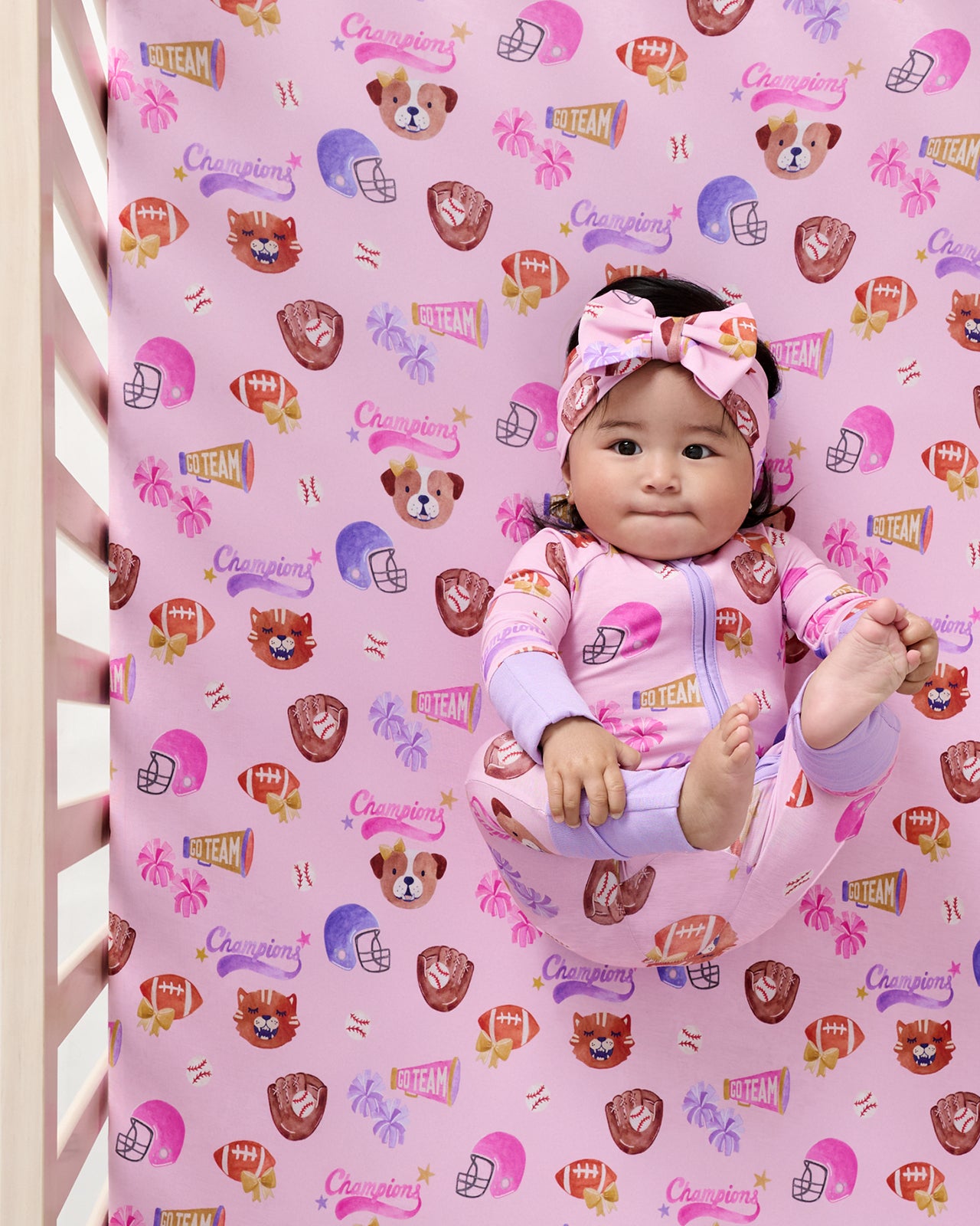 Aerial view of baby laying on the Team Spirit Pink Fitted Crib Sheet