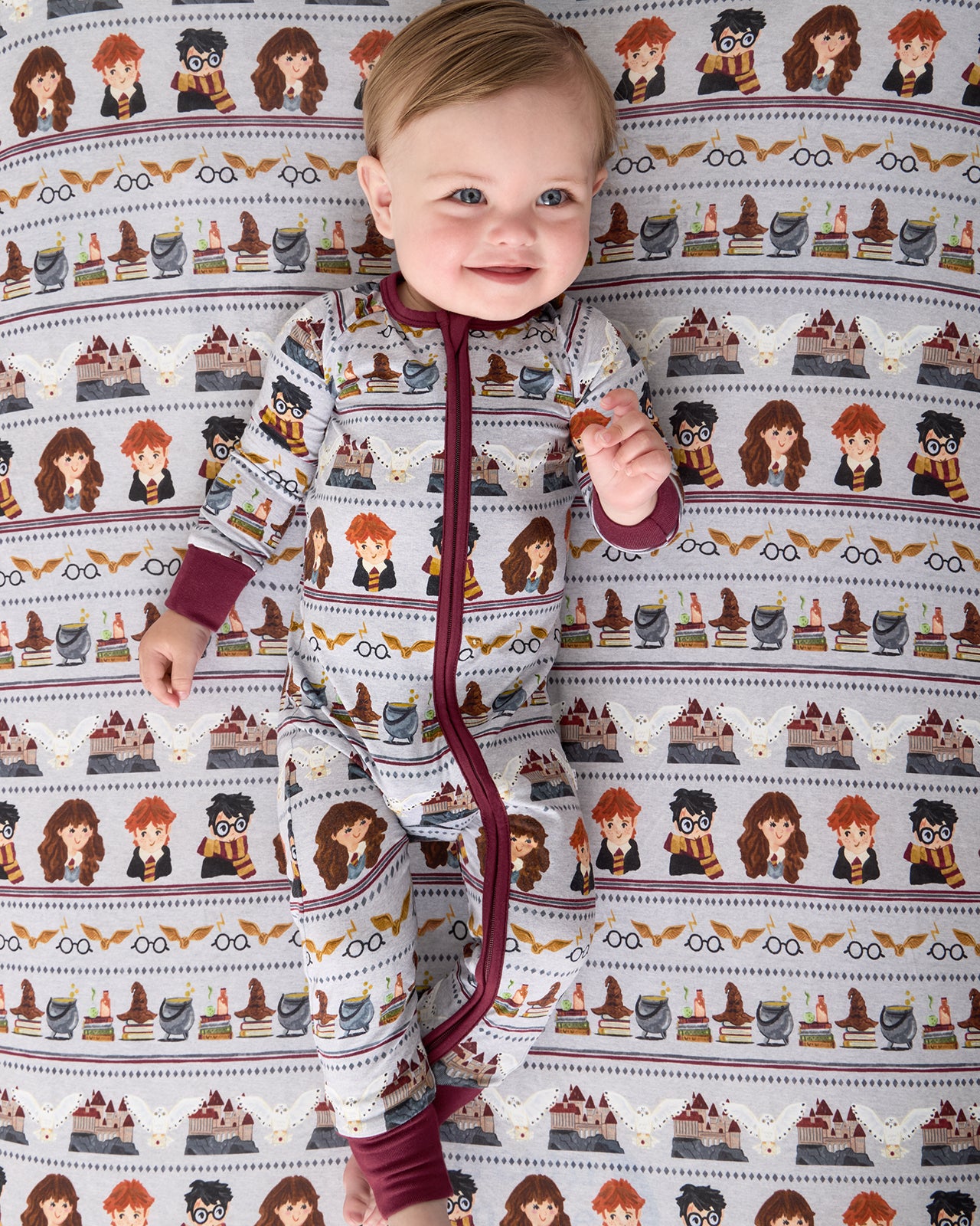 Aerial view of baby laying on the Harry Potter™ Spellbinding Studies Fitted Crib Sheet in a matching footie