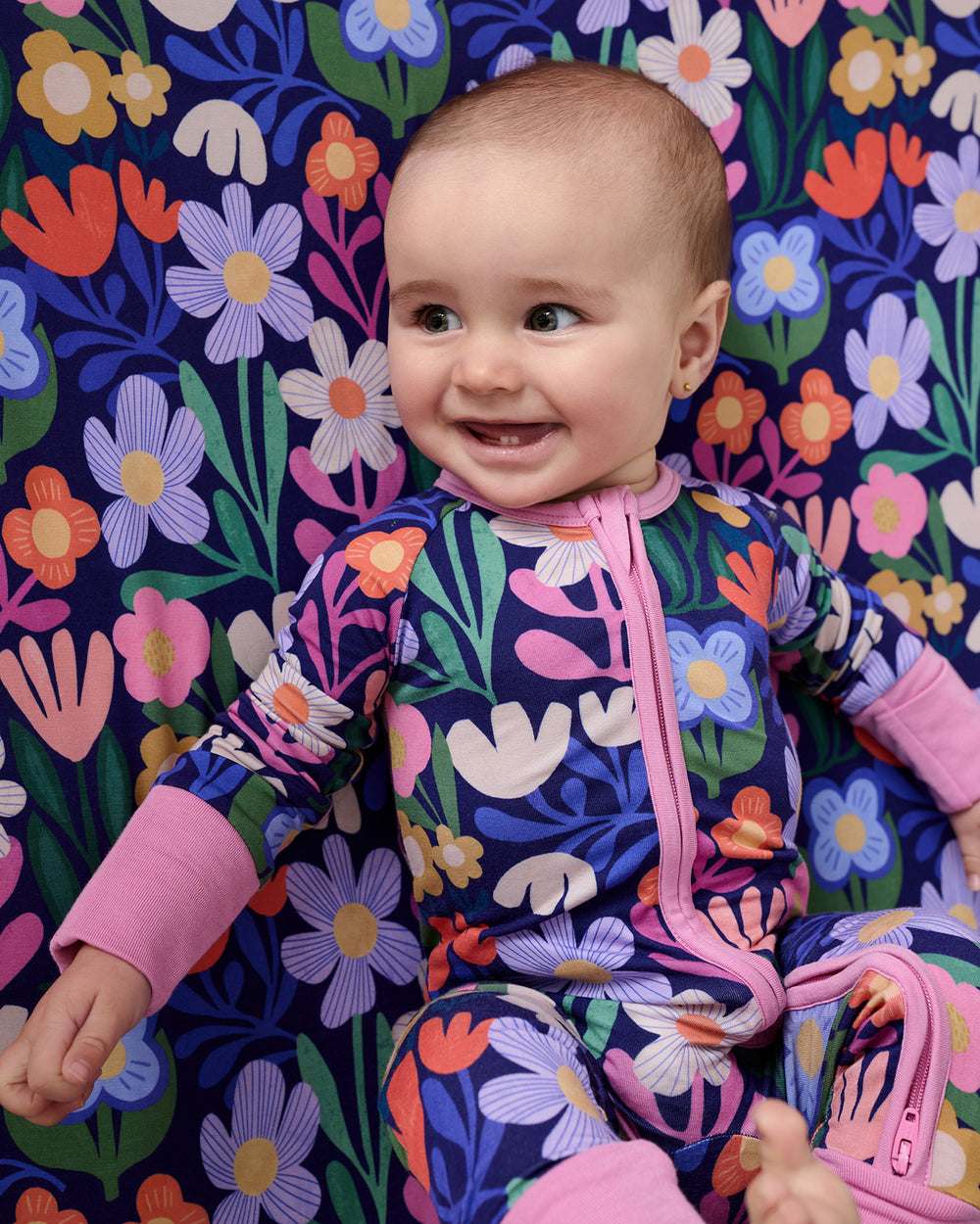 Close up of baby on the Wild Garden Fitted Crib Sheet wearing a matching zippy