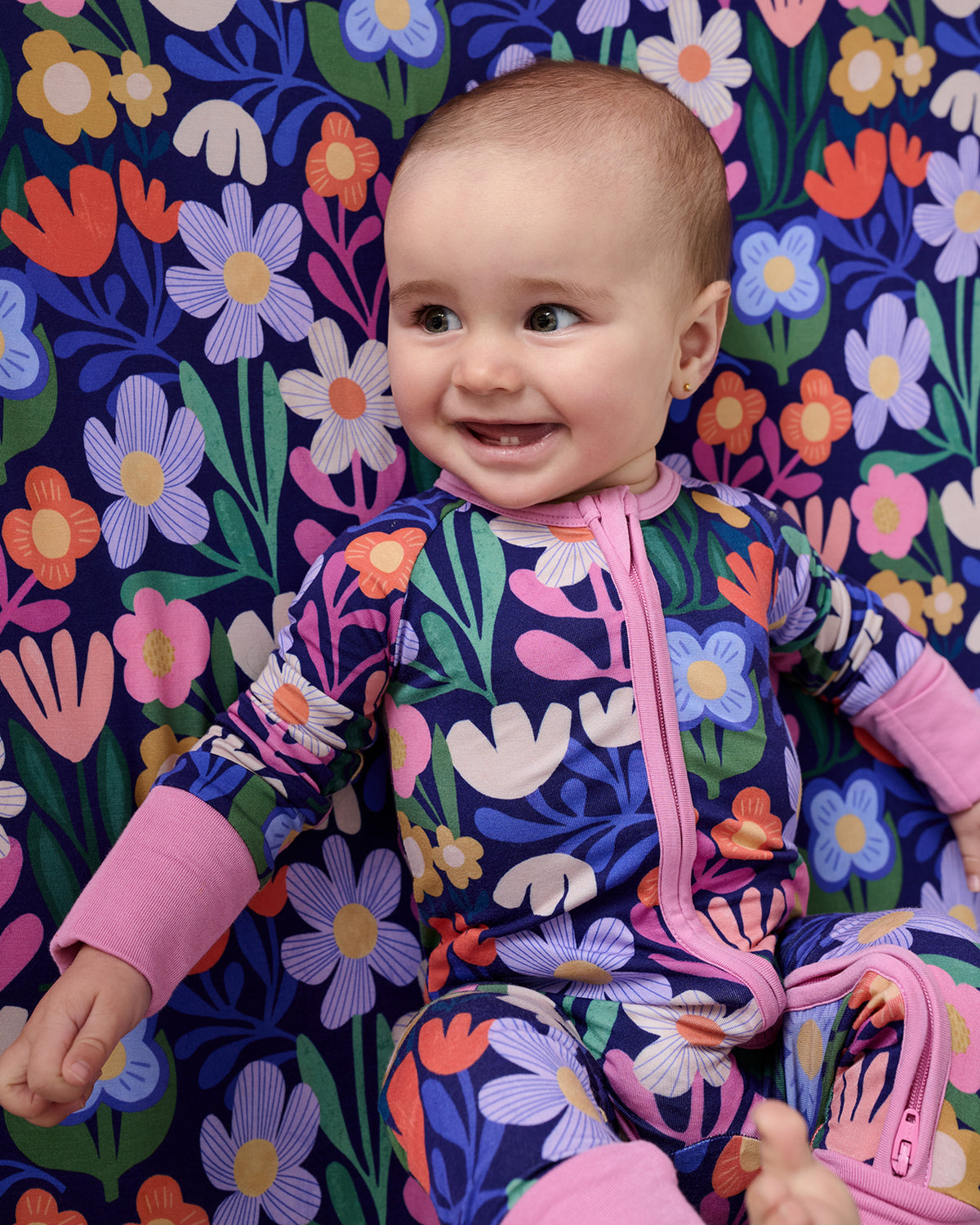Close up of baby on the Wild Garden Fitted Crib Sheet wearing a matching zippy