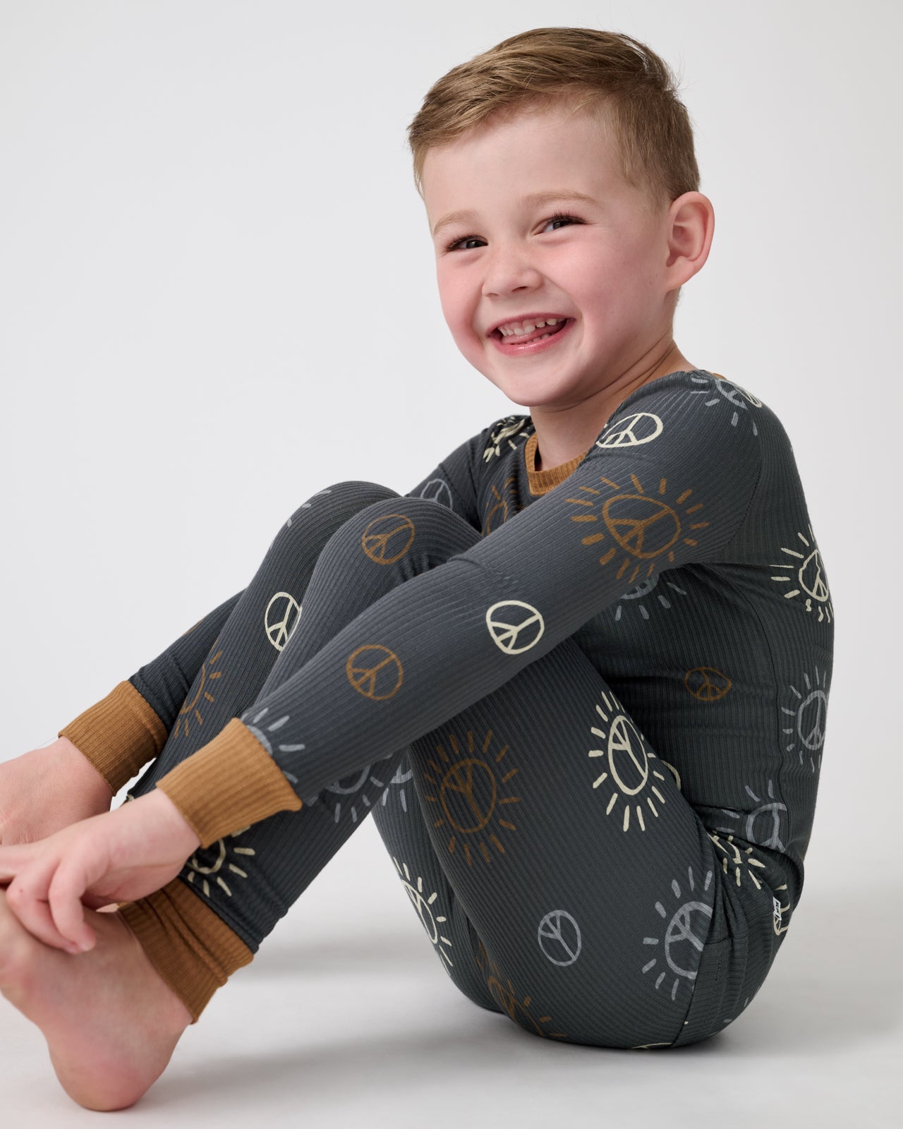 Sitting boy wearing the Peace & Love Ribbed Two-Piece Pajama Set