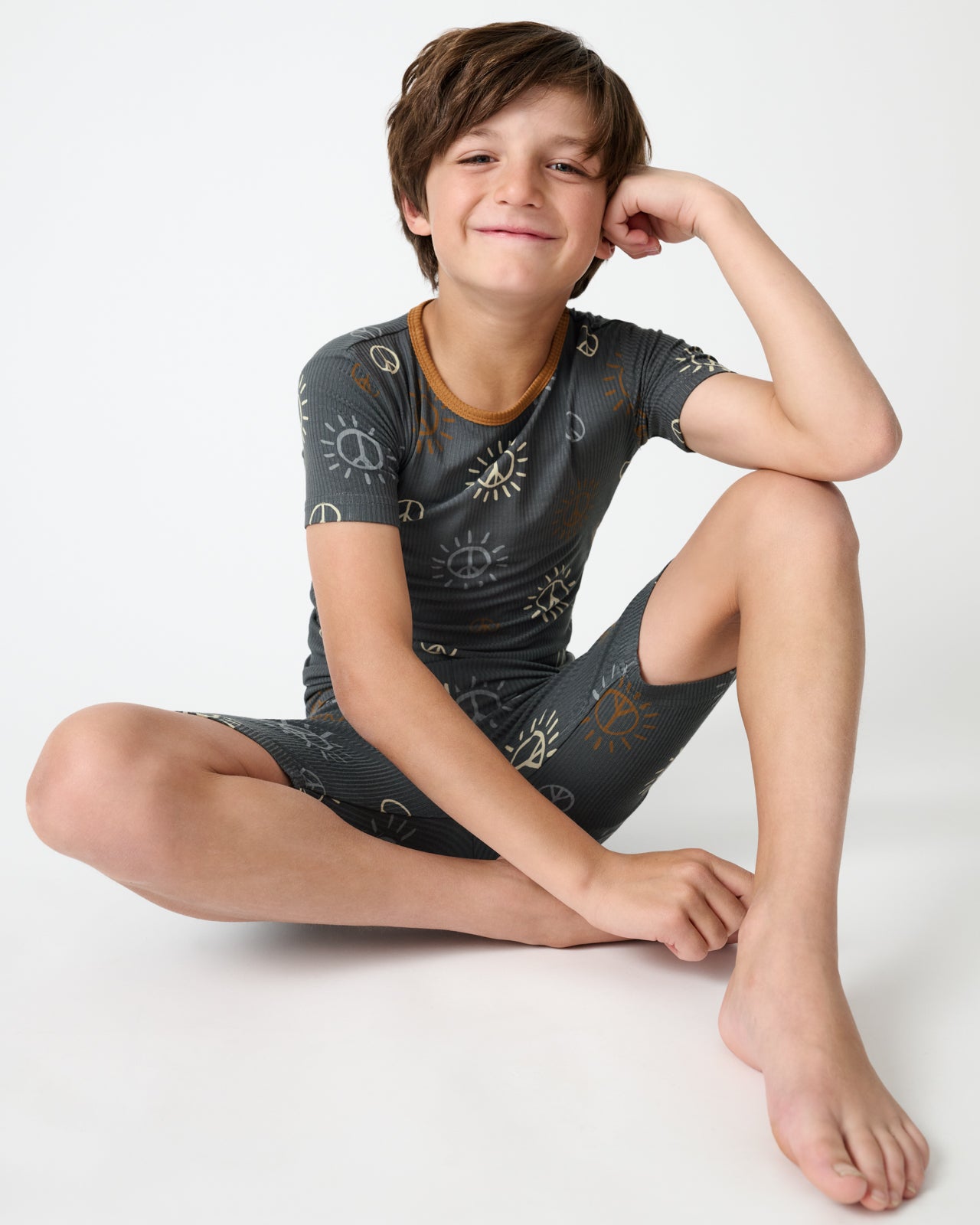 Sitting boy wearing the Peace & Love Ribbed Two-Piece Short Sleeve & Shorts Pajama Set