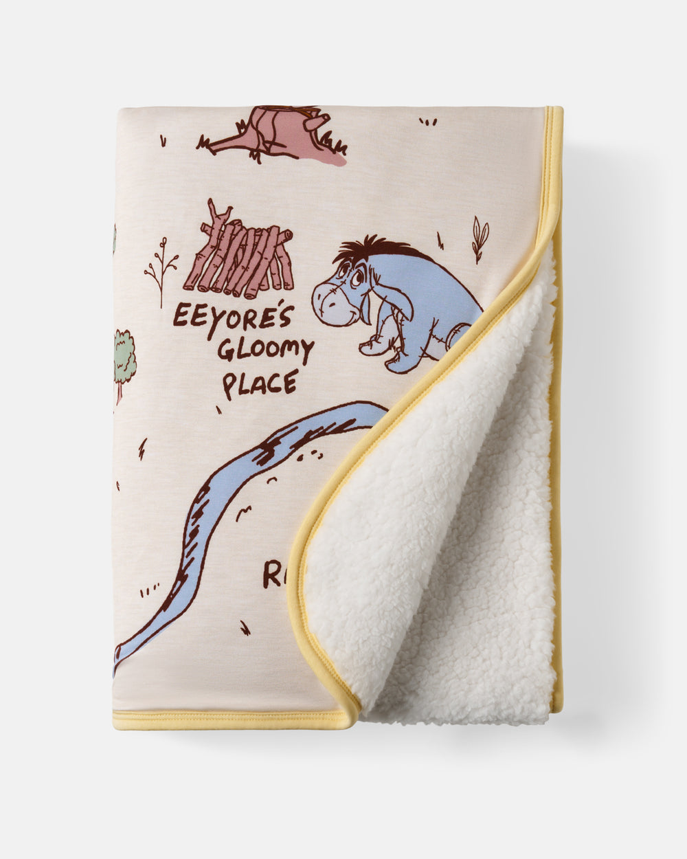 A folded fleece throw blanket featuring Winnie the Pooh character artwork, including Eeyore and the text 'Eeyore's Gloomy Place,' with a cream sherpa lining and yellow trim, shown on a light gray background.