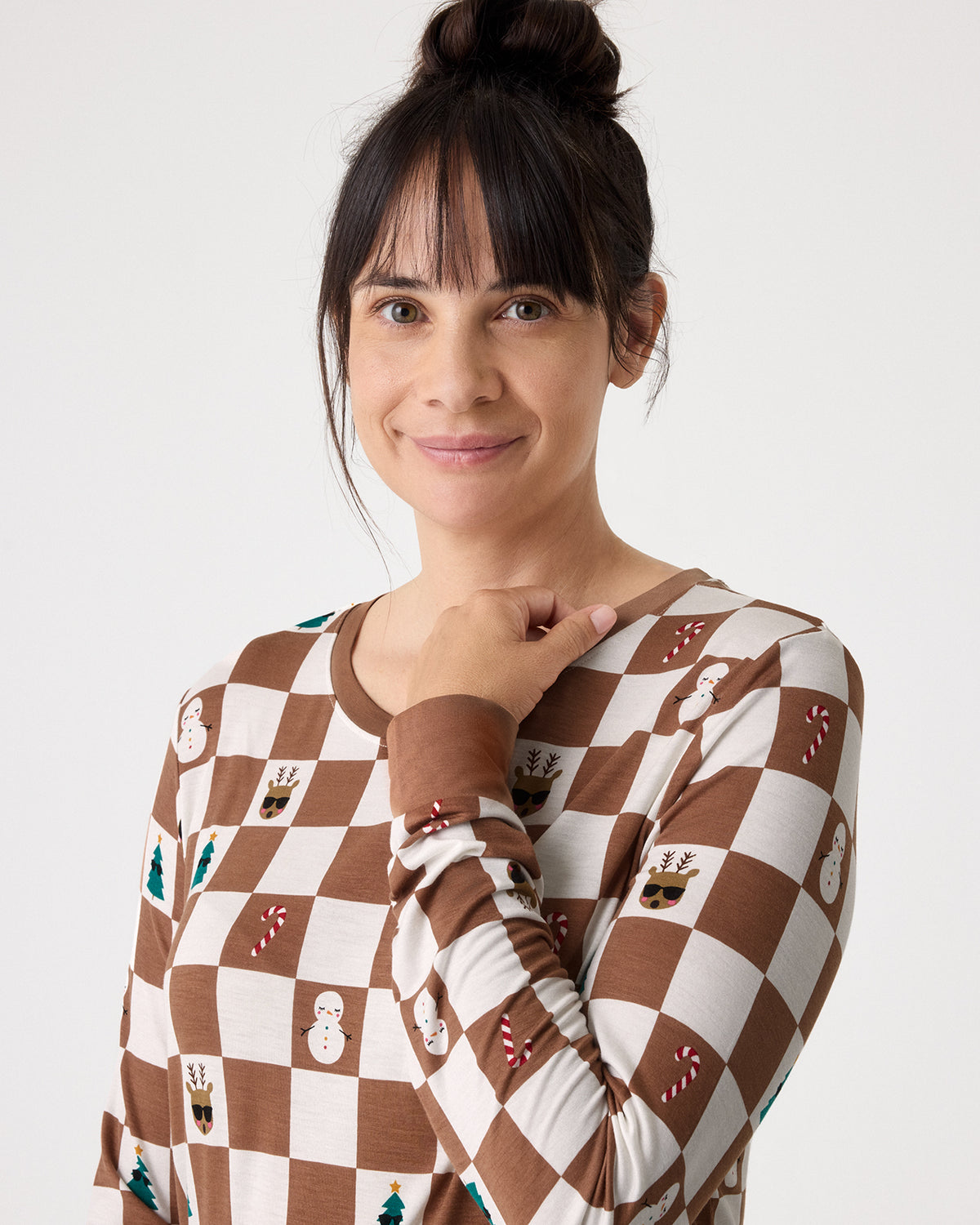 A woman wearing a brown and cream checkered long-sleeve shirt with small holiday-themed motifs, photographed against a plain light gray background.