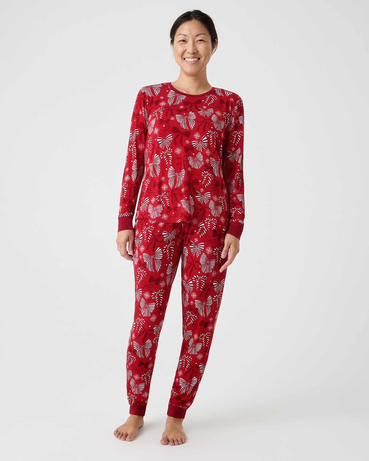 A woman modeling a two-piece long-sleeve pajama set with a red and white bow pattern, standing against a light studio background.