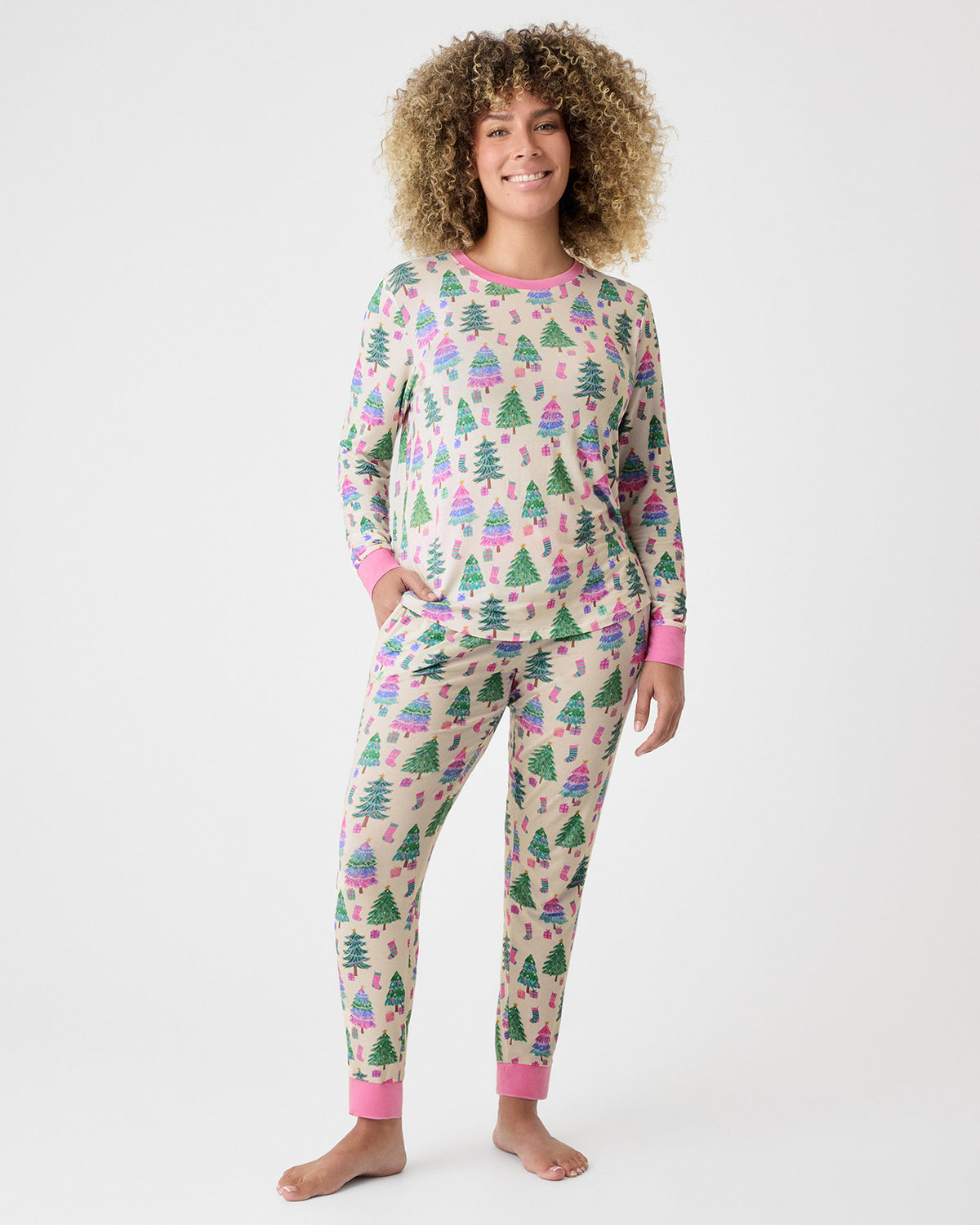 A woman modeling a two-piece long-sleeve pajama set with a Christmas tree print on a beige background with pink cuffs and collar.