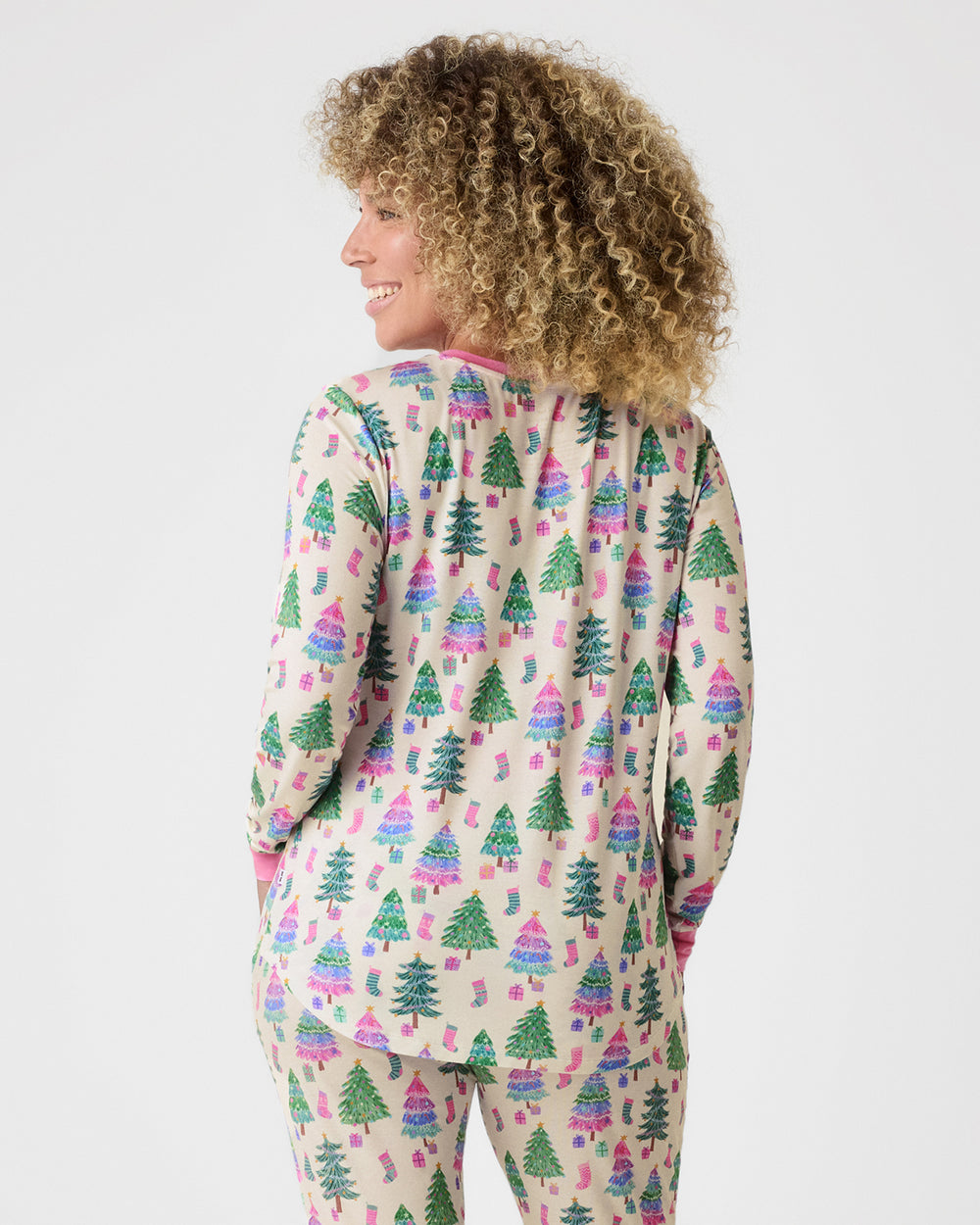 A woman shown from the back wearing a matching long-sleeve pajama set with a Christmas tree print on a light beige background.