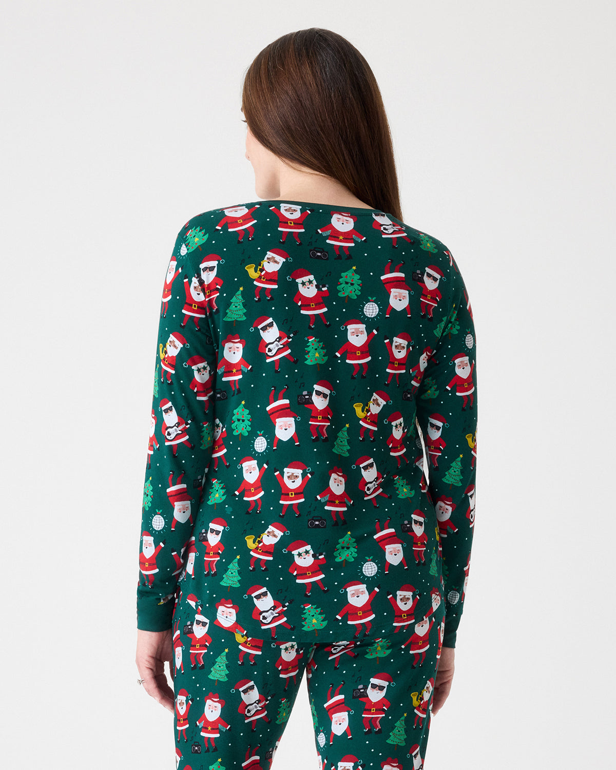 A woman shown from the back wearing a dark green long-sleeve pajama set with an all-over Santa Claus print, against a plain light gray studio background.