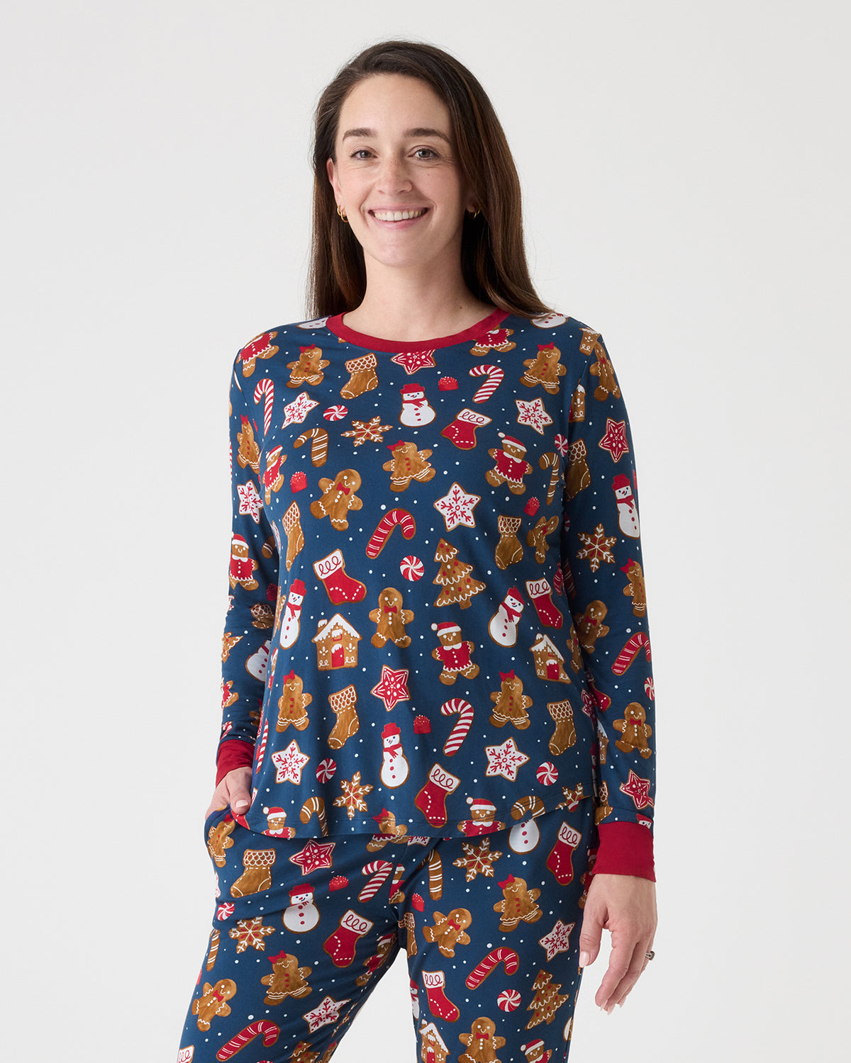 A woman modeling a matching long-sleeve pajama set with a festive Christmas print on a solid light gray background.