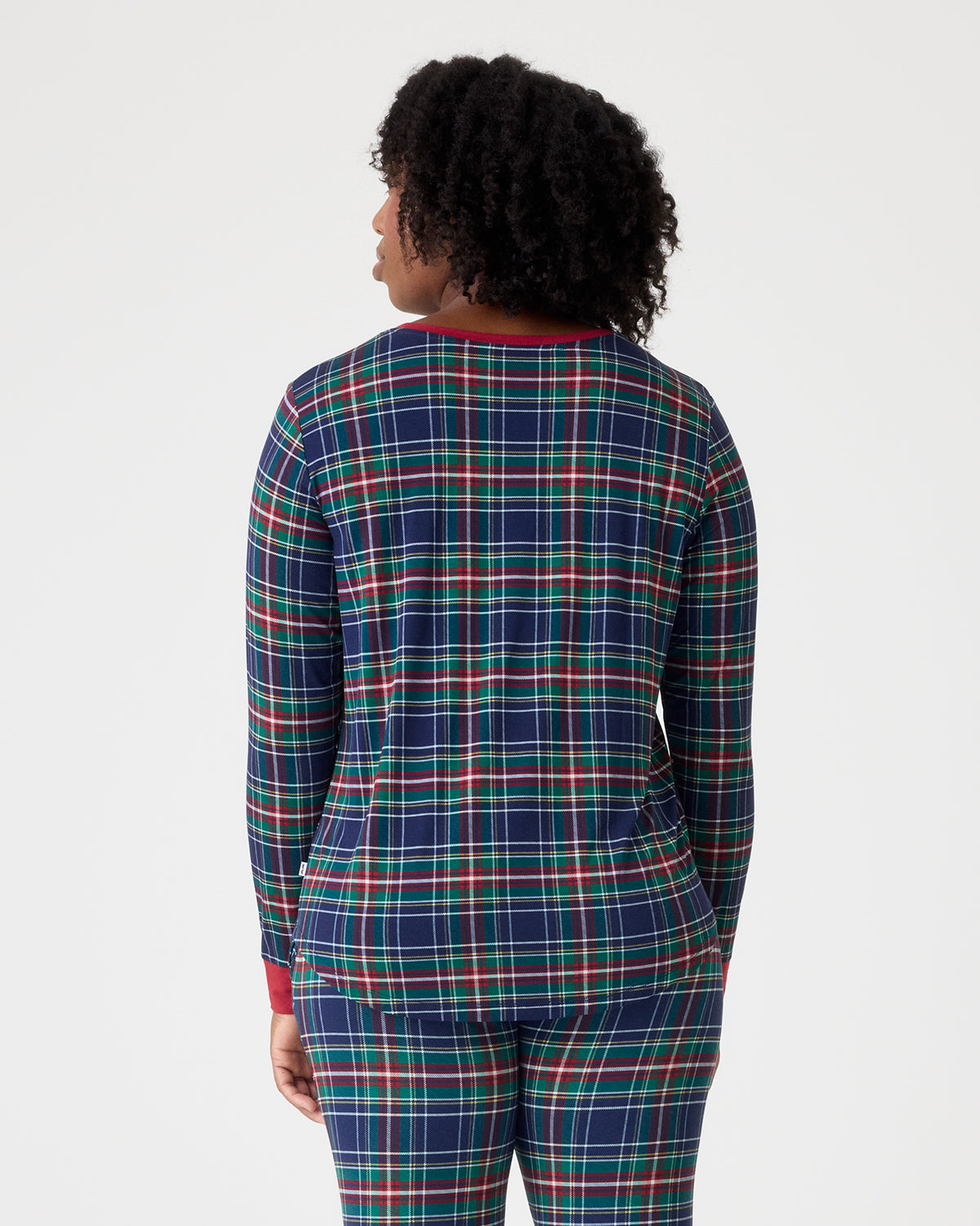 A person shown from the back wearing a long-sleeve plaid pajama top and matching pants in navy blue with red and green lines, against a light gray studio background.
