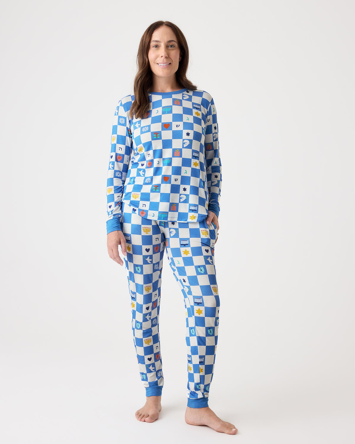 A woman modeling a matching long-sleeve pajama set with a blue and white checkerboard pattern and small colorful motifs, standing against a plain light gray studio background.