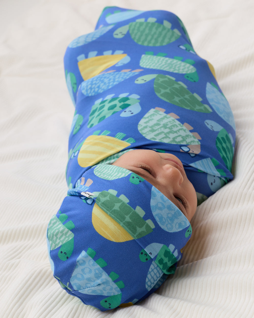 Baby wrapped in the Shell Parade Swaddle & Hat Set on a white blanket