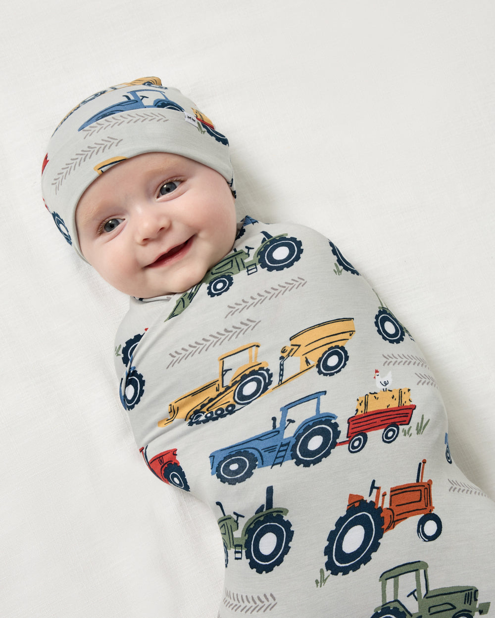 Close up of baby boy wrapped in the Tractor Tales Swaddle & Beanie Set