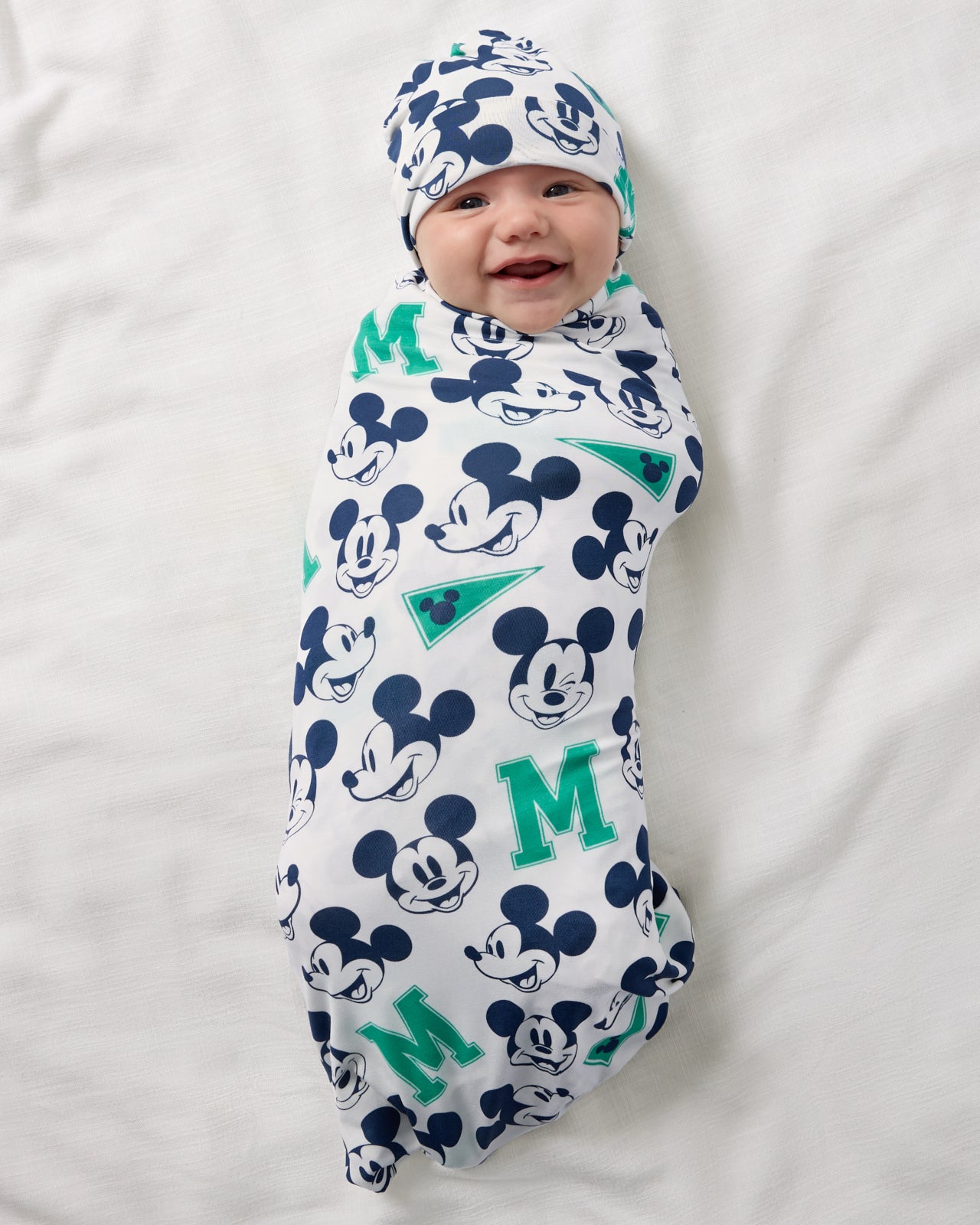 Aerial view of baby wrapped in the Disney Varsity Mickey Mouse Swaddle & Beanie Set