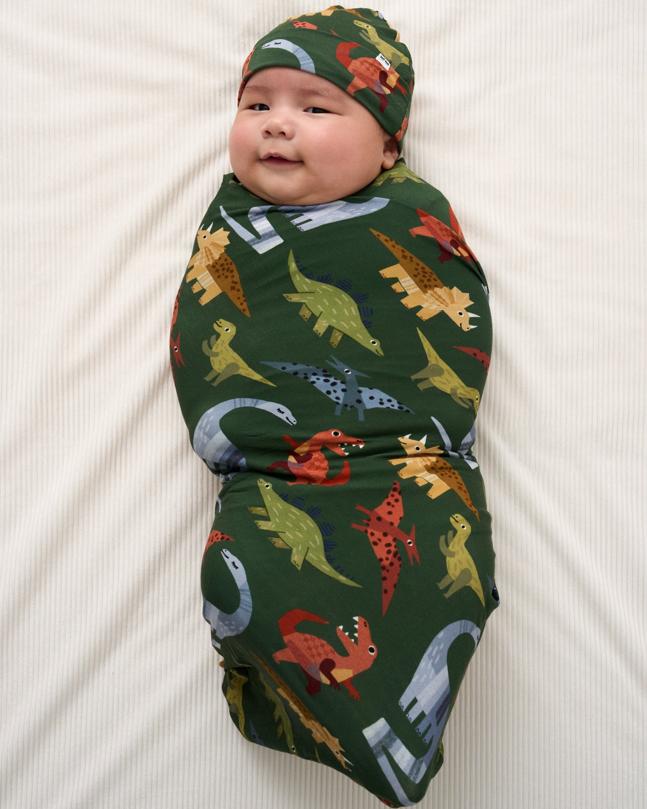 Aerial view of baby wearing the Green Roar & Explore Swaddle & Beanie Set