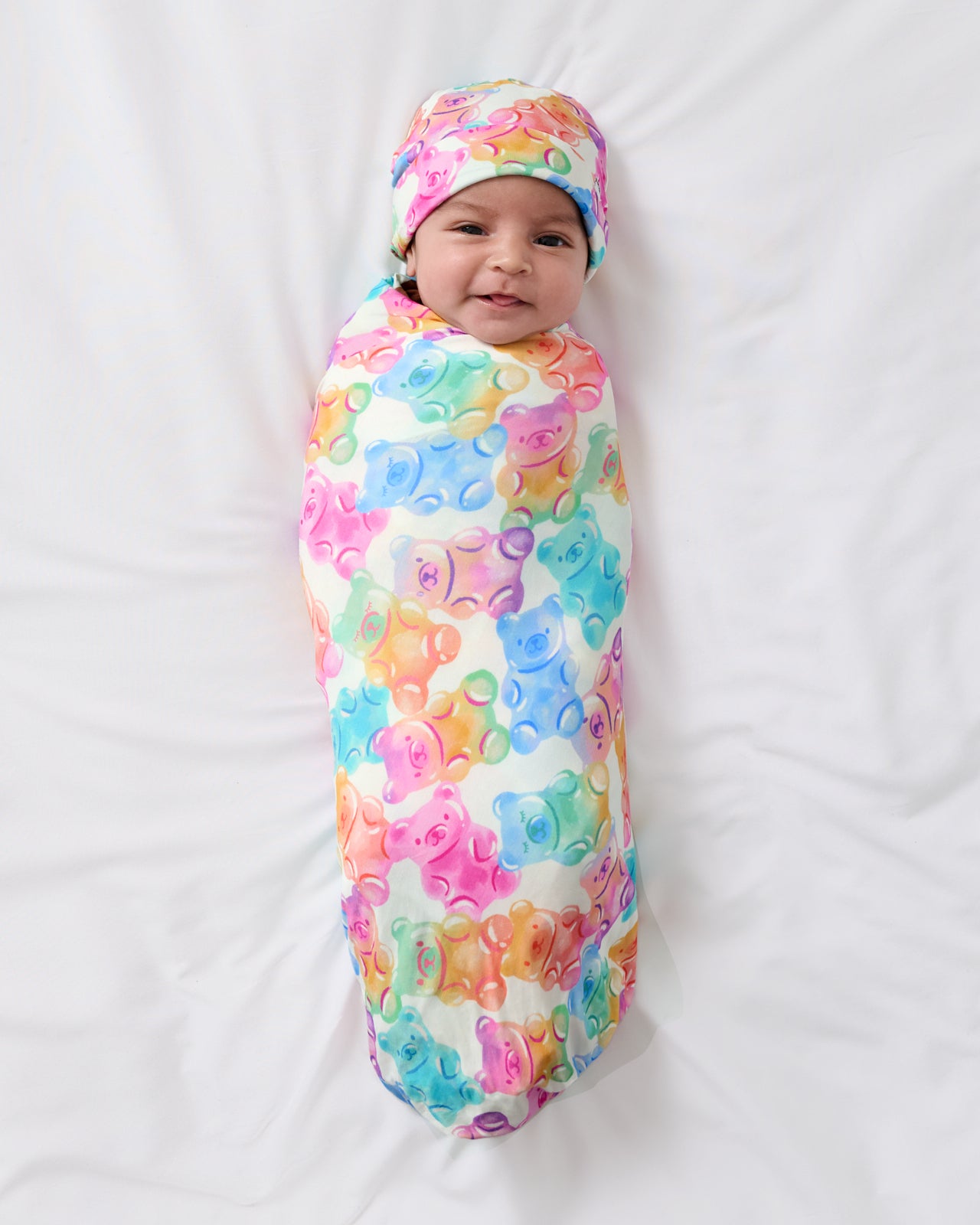 Aerial view of baby wearing the Gummy Giggles Swaddle & Beanie Set