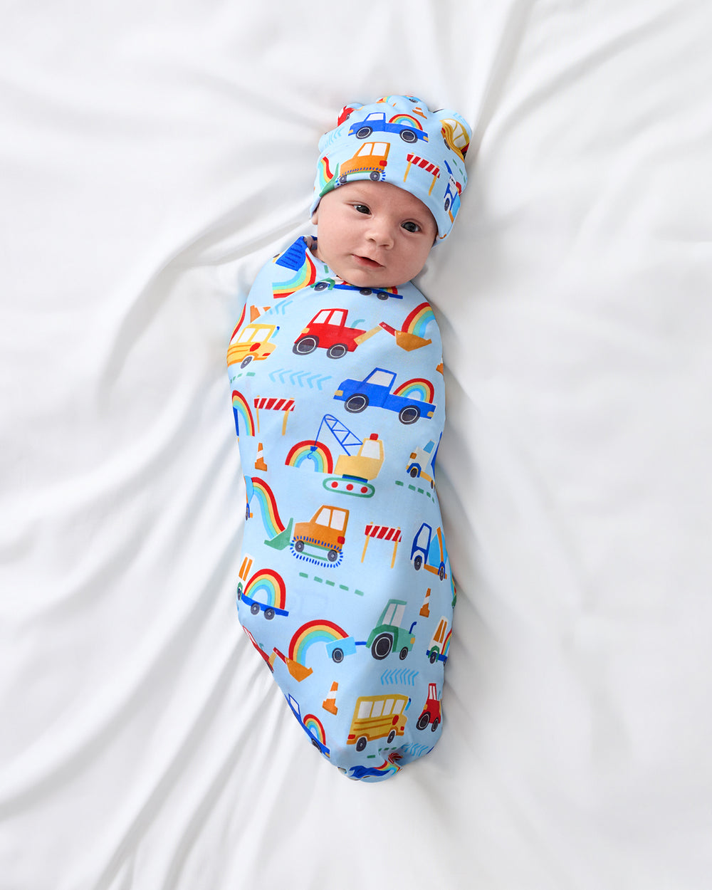 Aerial view of baby wrapped in the Rainbow Trucks Swaddle & Beanie Set