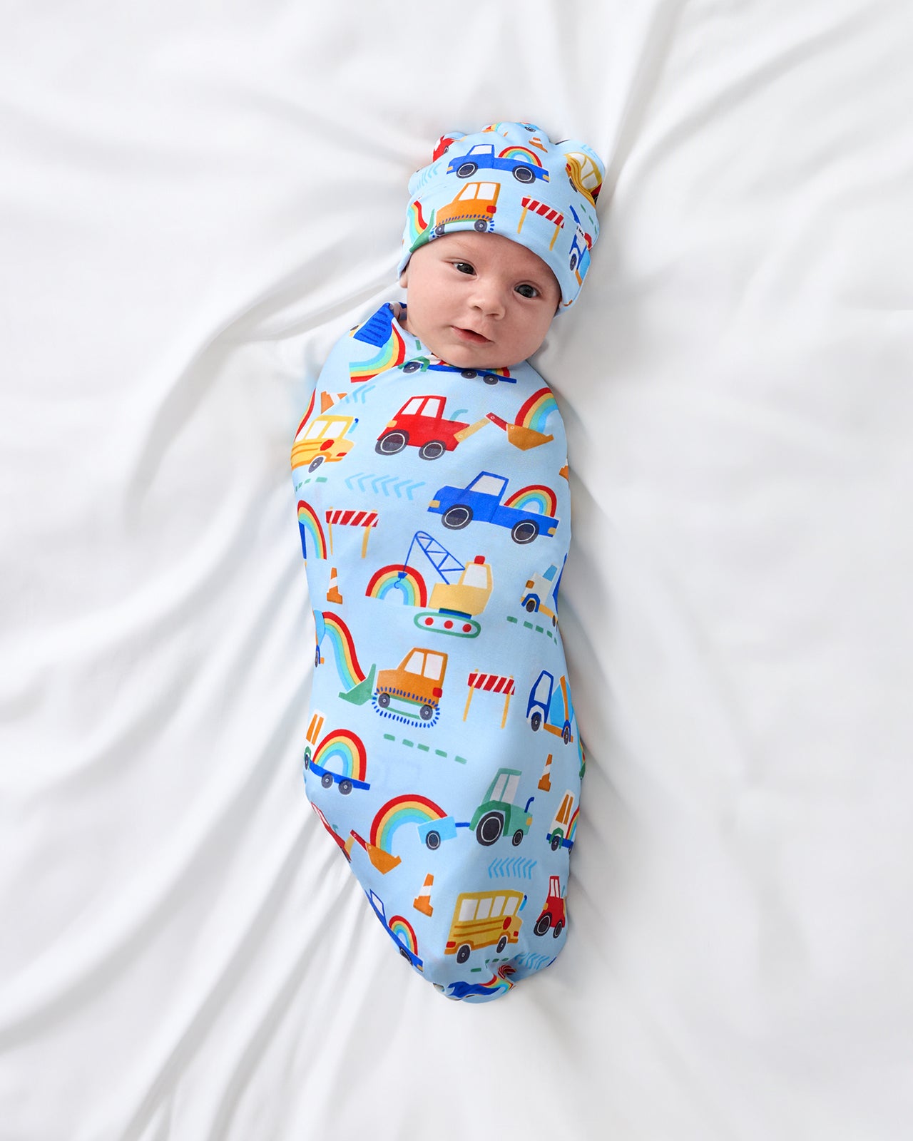 Aerial view of baby wrapped in the Rainbow Trucks Swaddle & Beanie Set