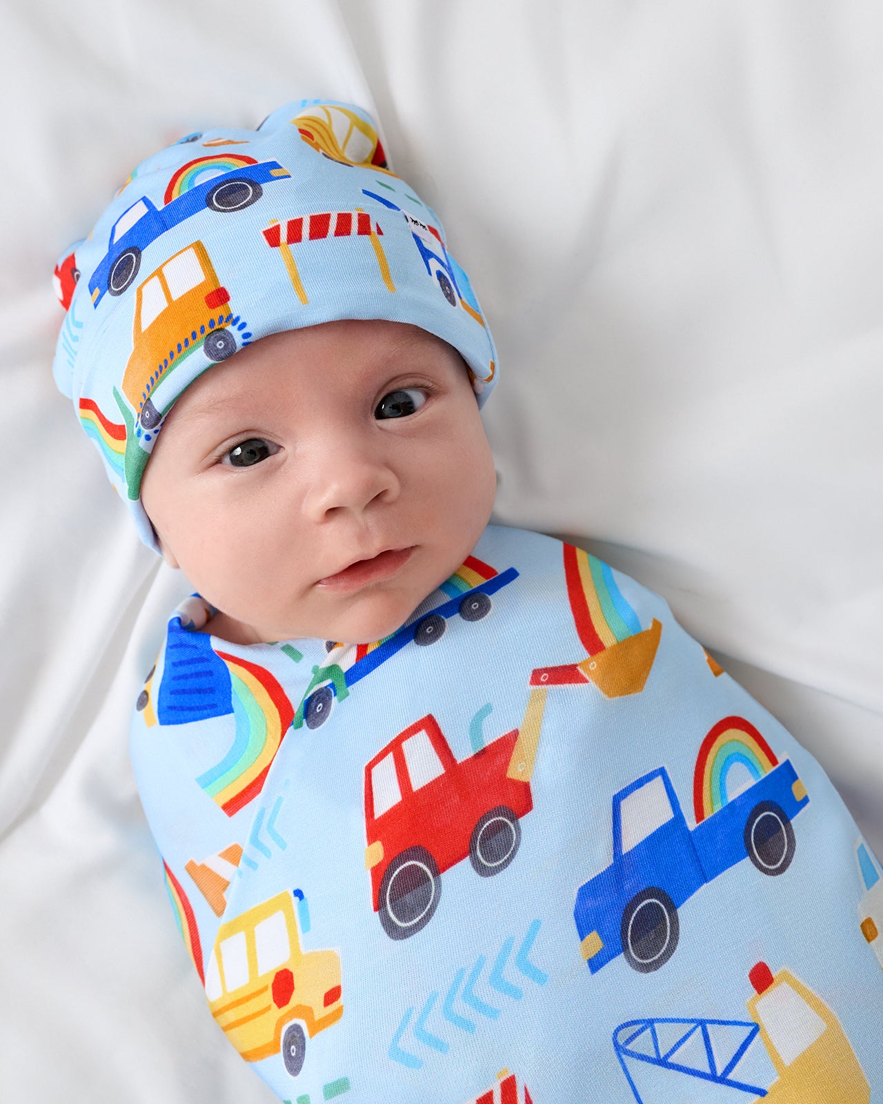 Close up of baby wearing the Rainbow Trucks Swaddle & Beanie Set