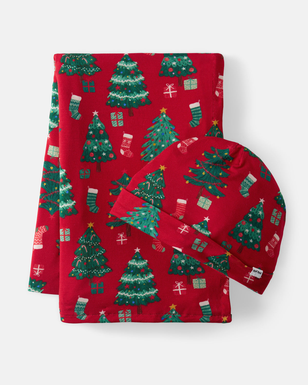 A folded red blanket set with a Christmas tree and stocking pattern, including a blanket and hat, photographed on a light gray background.