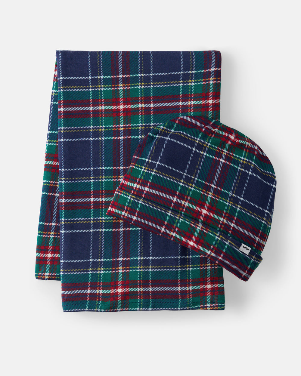 A folded plaid blanket and a matching beanie hat in a navy tartan pattern with green, red, and white stripes, photographed on a light gray background.