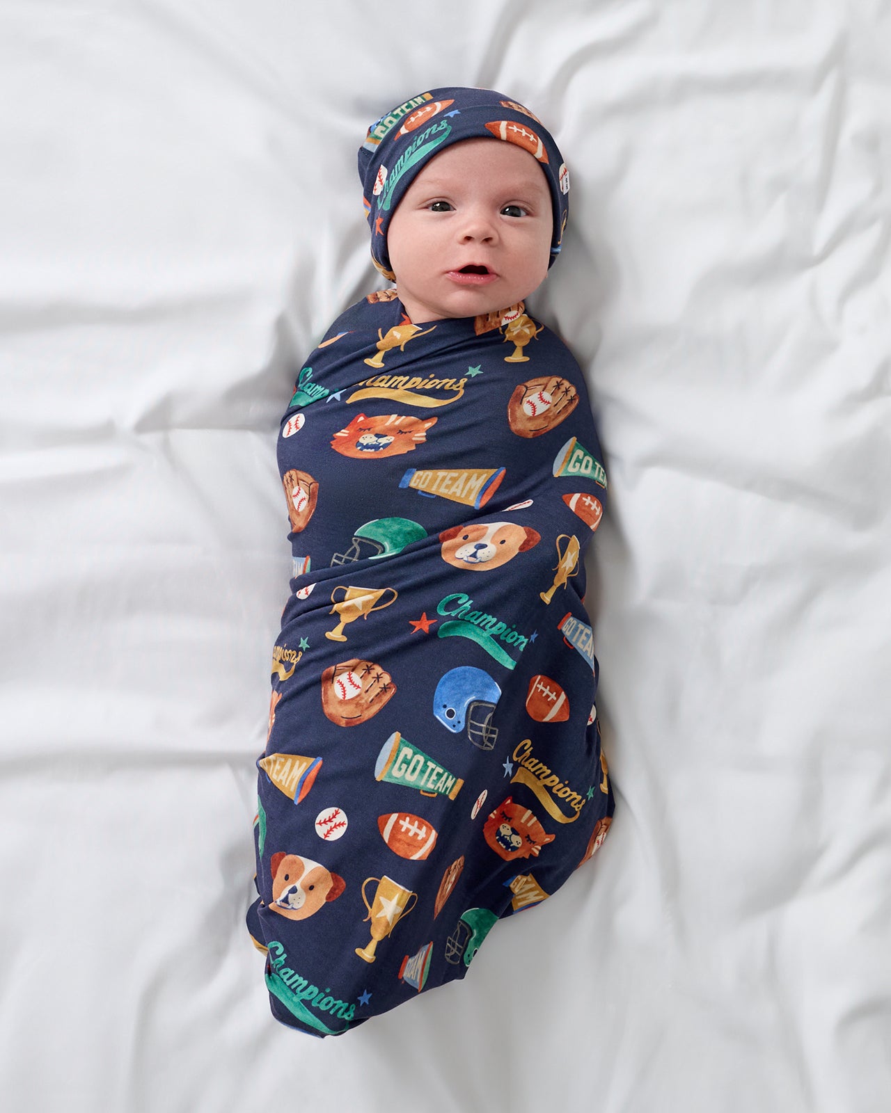 Aerial view of baby wrapped in the Team Spirit Swaddle & Beanie Set