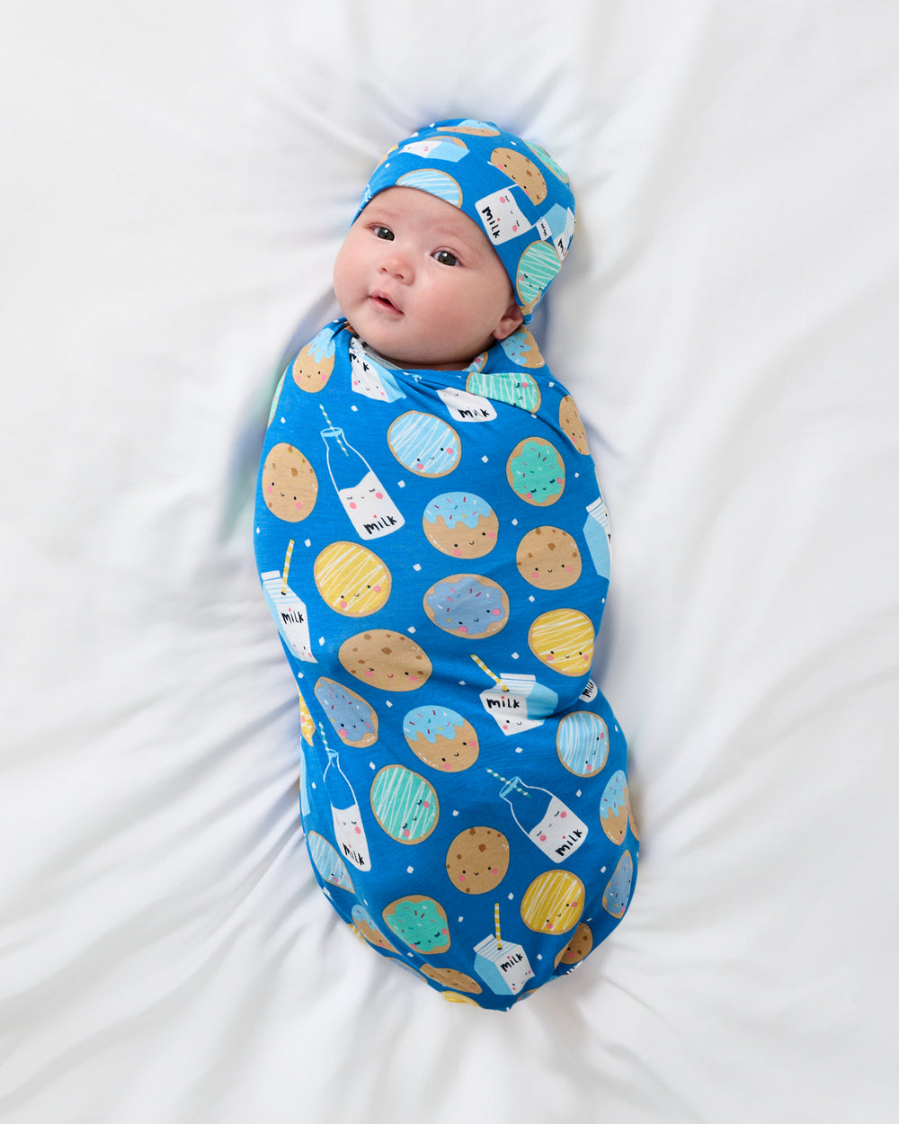 Aerial view of newborn wrapped in the Blue Cookies & Milk Swaddle & Beanie Set