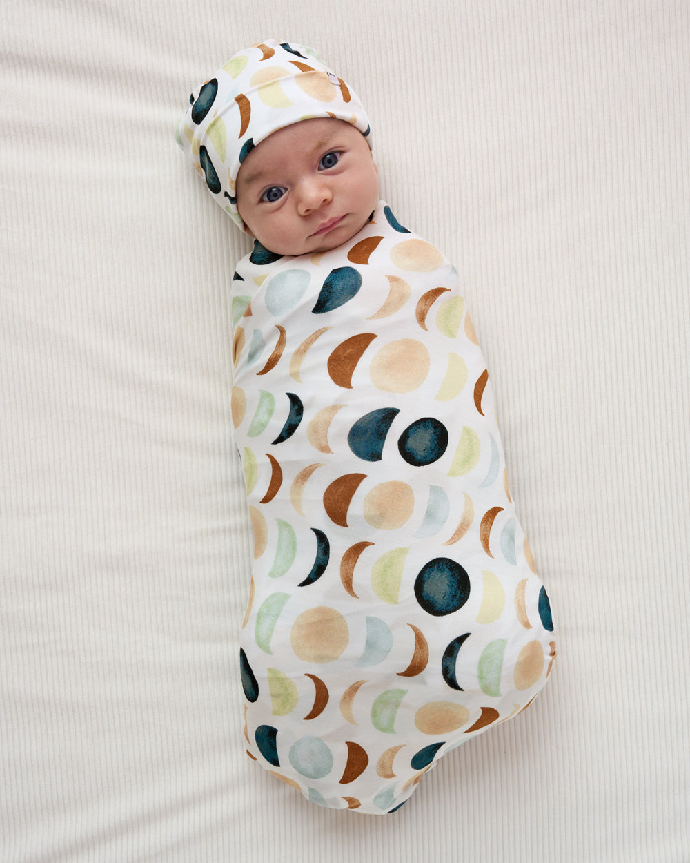Aerial view of baby wearing the Luna Neutral Swaddle & Beanie Set