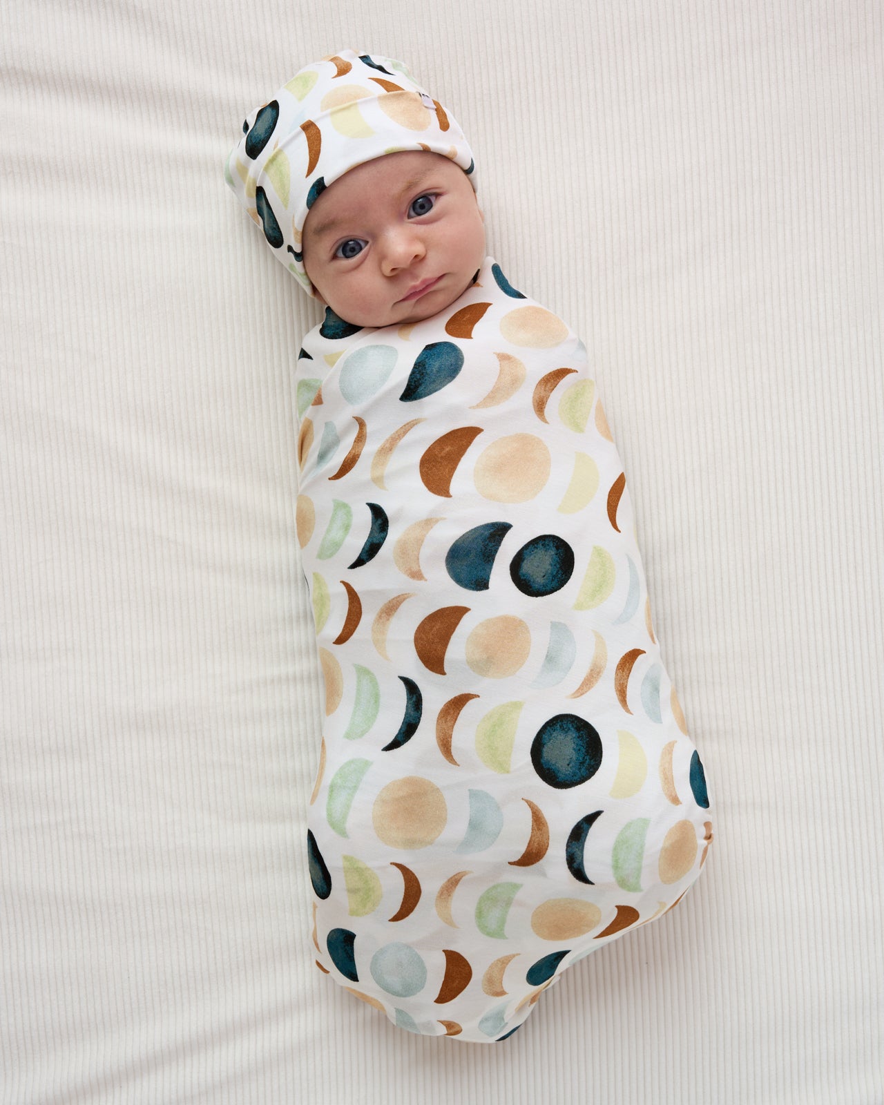 Aerial view of baby wearing the Luna Neutral Swaddle & Beanie Set