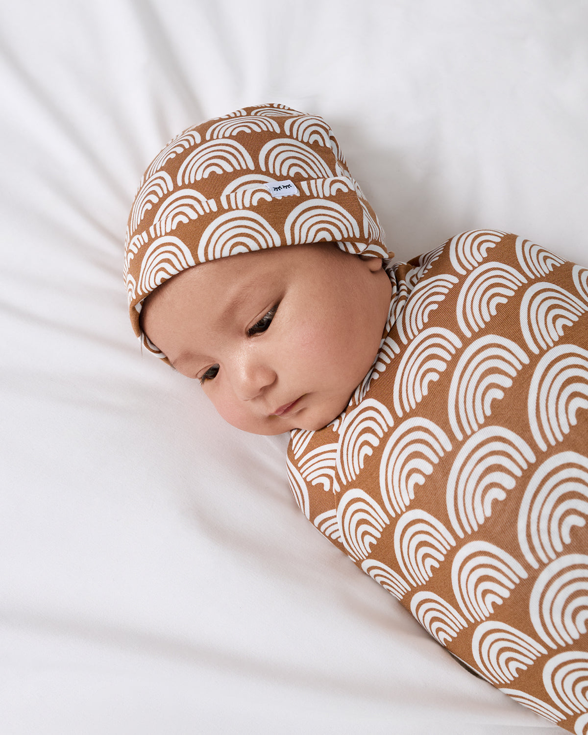 Close up of baby wearing the Rust Rainbows Swaddle & Beanie Set